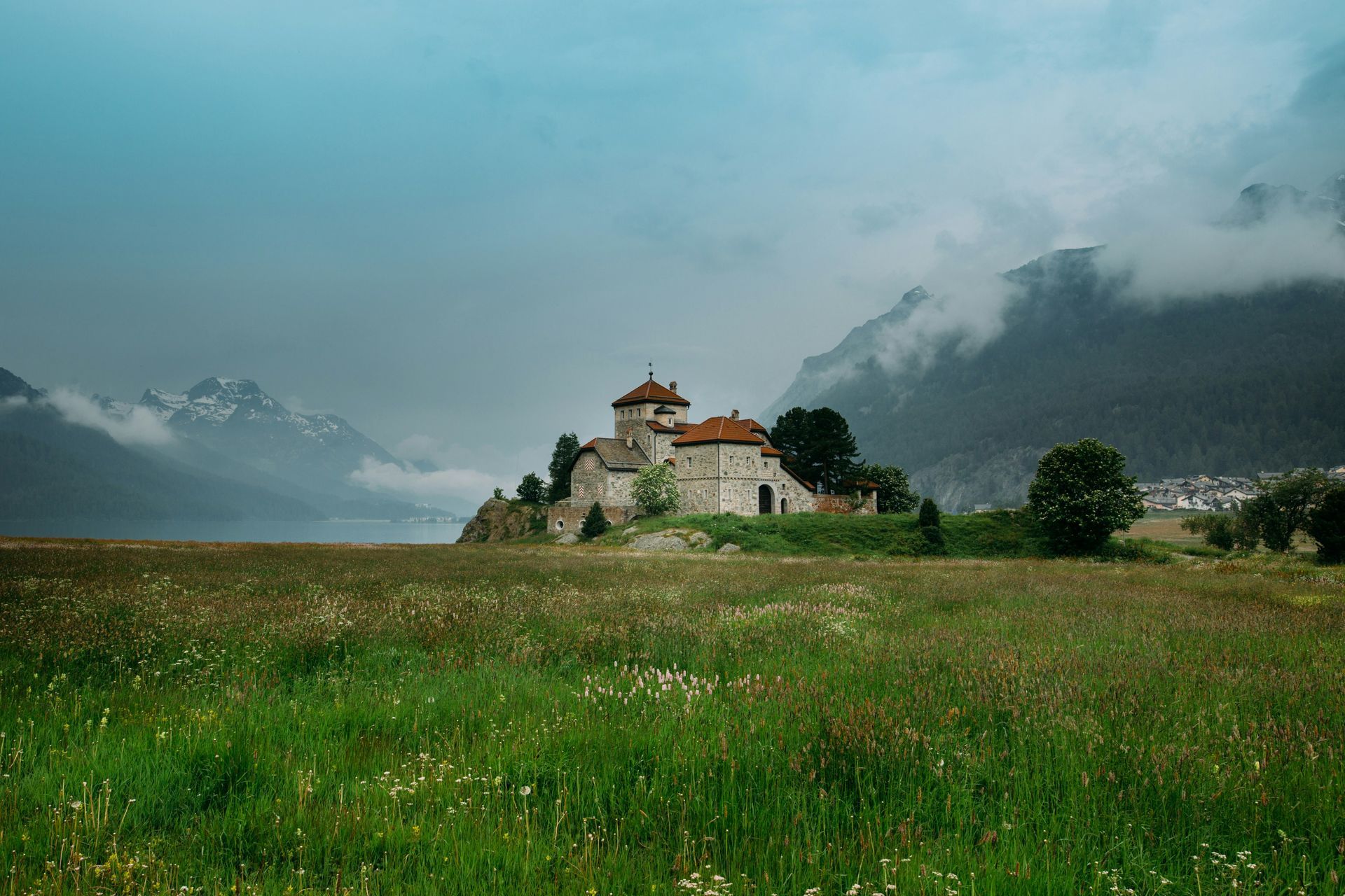 Castle on a grassy hill, with mountains and clouds in the background, in St. Moritz, Switzerland.