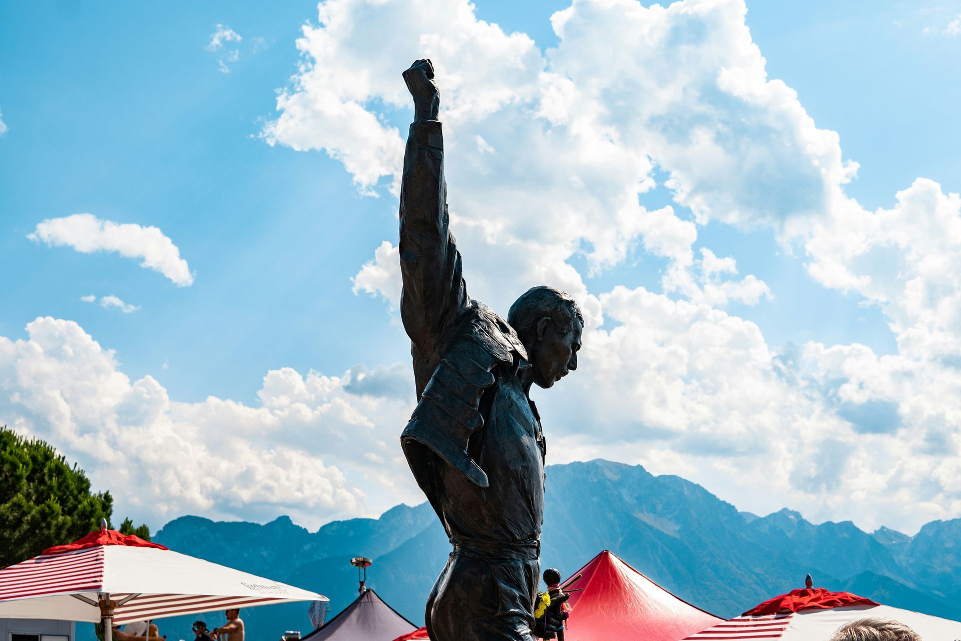Bronze statue of Freddie Mercury with raised fist, set against mountains and a cloudy sky in Montreux, Switzerland.