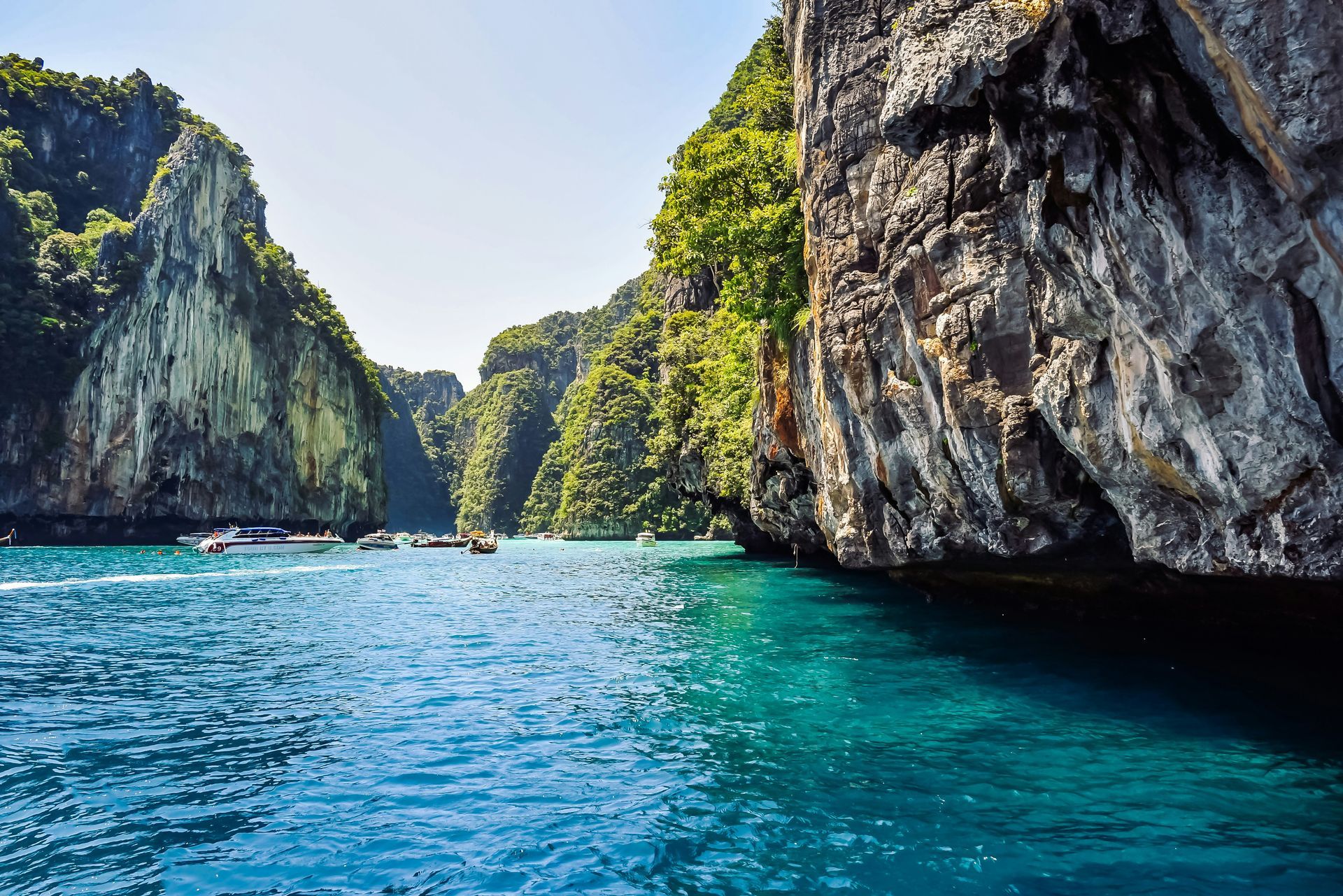 A group of boats are floating on top of a body of water surrounded by he Phi Phi Islands in Krabi, Thailand.