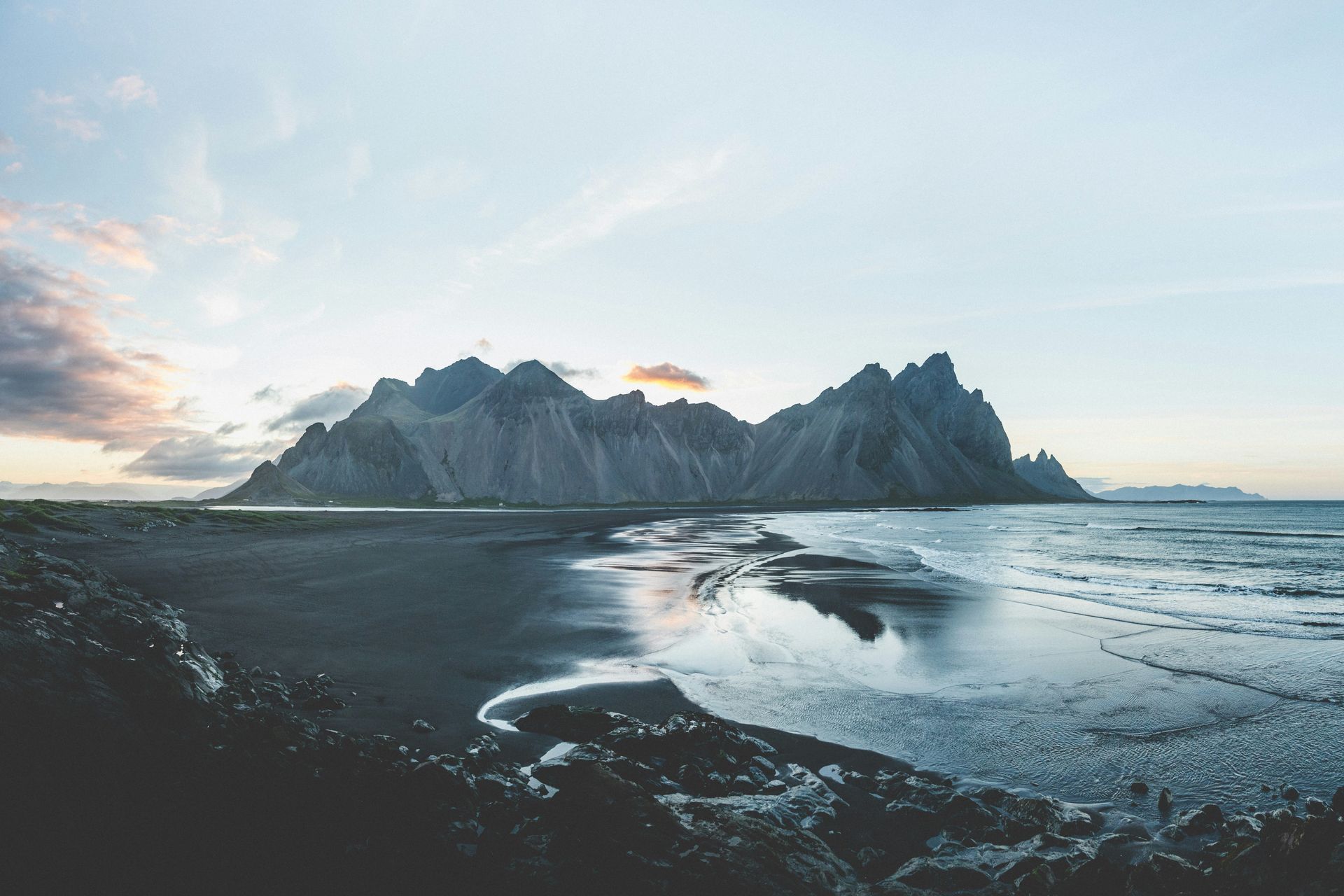 Black sand beach with dark mountains and ocean under a cloudy sky in Stokksnes, Iceland.