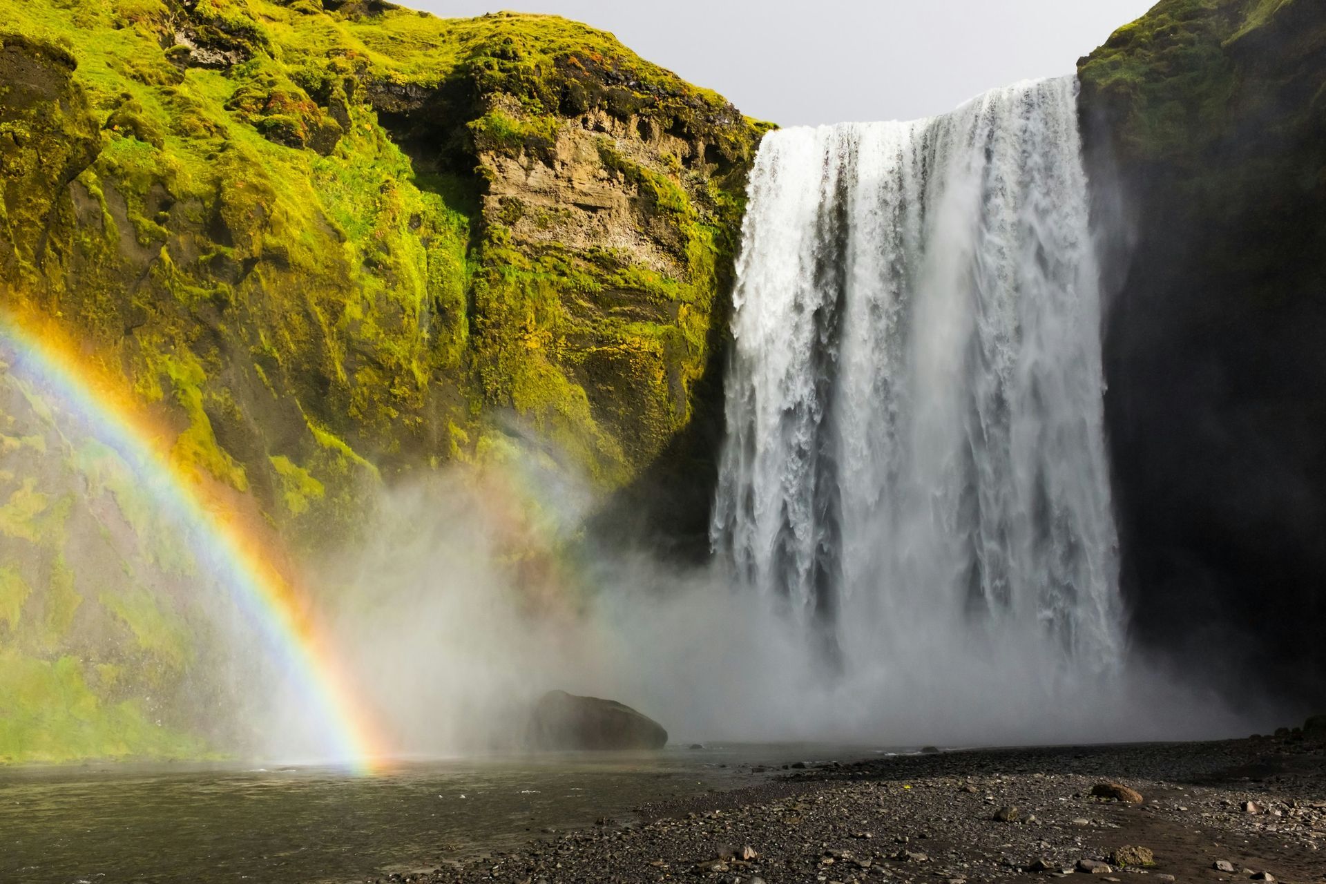 Skógafoss Waterfall cascading down into a misty pool, creating a rainbow in Iceland.