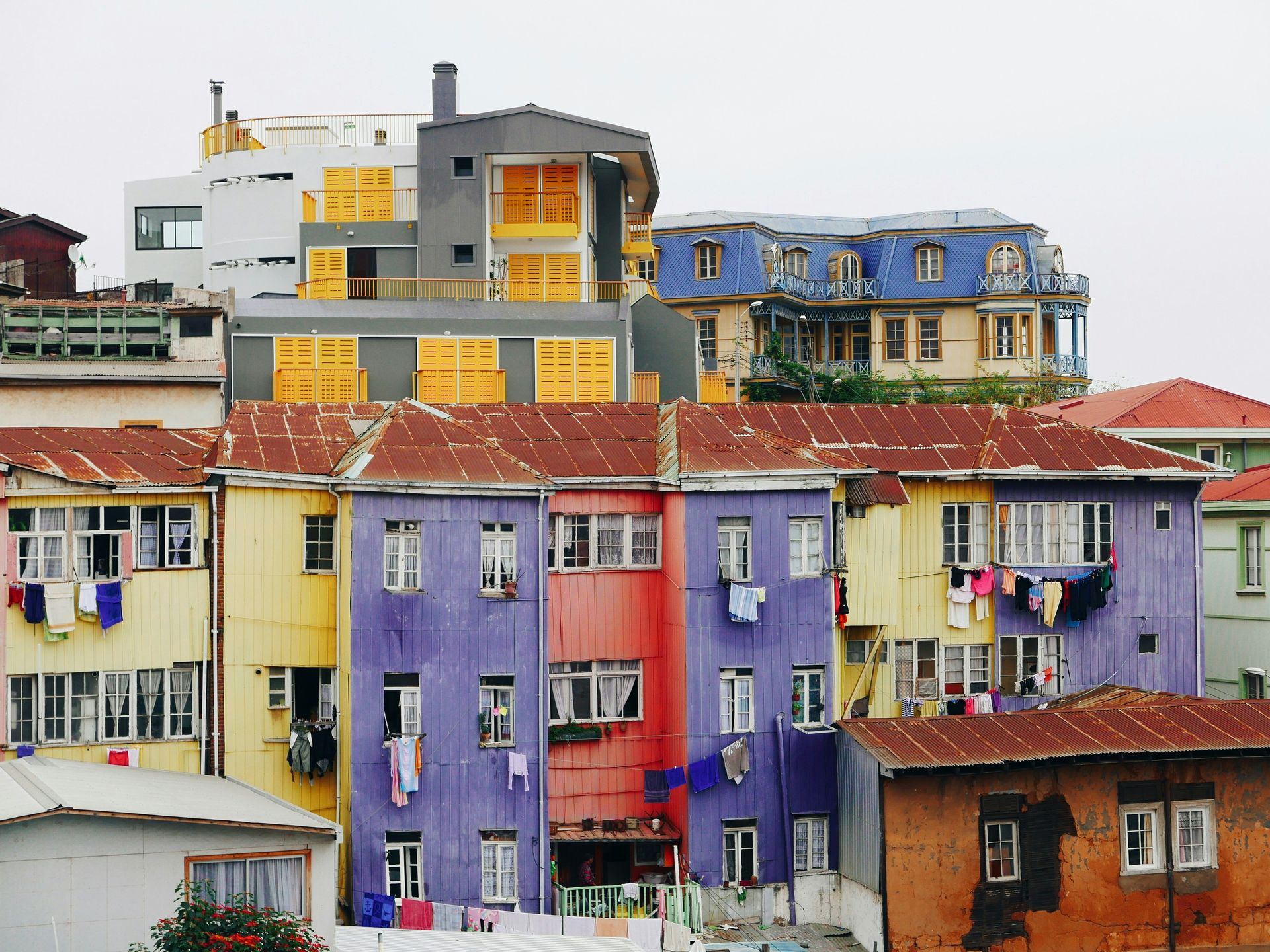 Colorful buildings on a hillside, laundry hangs.  Bright hues of purple, yellow, and blue against an overcast sky in Valparaíso, Chile.