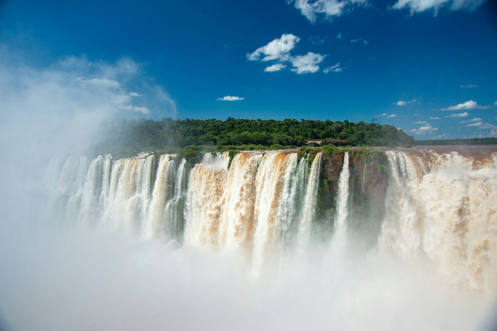 Iguazu Falls, a massive waterfall cascade; water plunges over a cliff into mist, with blue sky and clouds in Argentina.