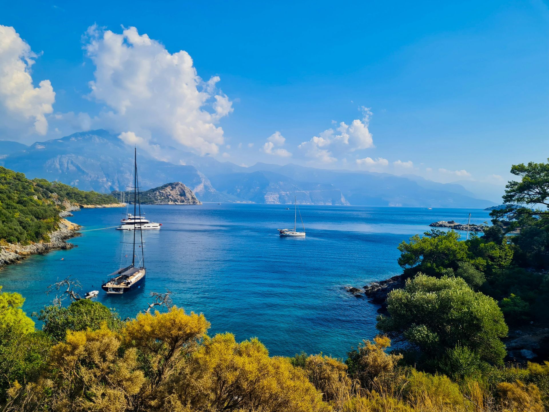 Sailboats on turquoise sea, framed by trees and mountains in Fethiye, Turkey.