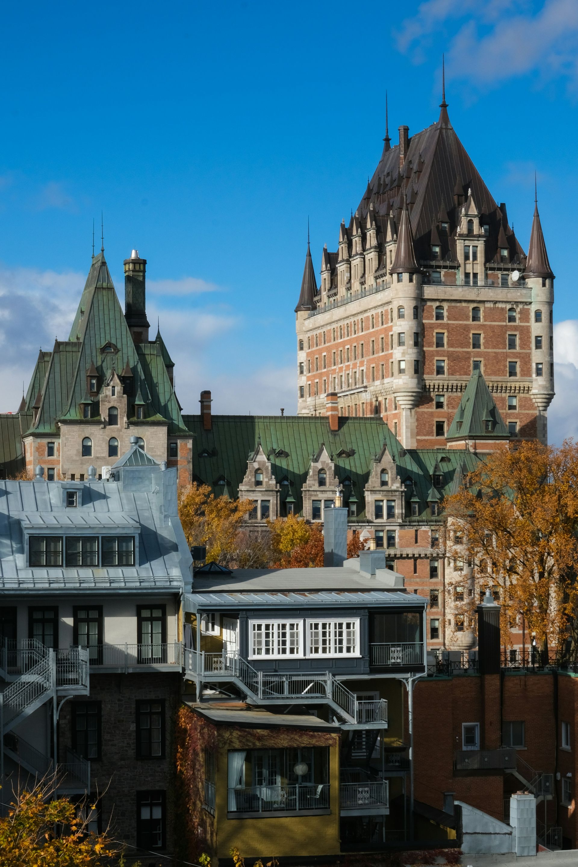 Buildings of Old Quebec City, with the Chateau Frontenac prominent in the background. Colorful rooftops and a clear blue sky.