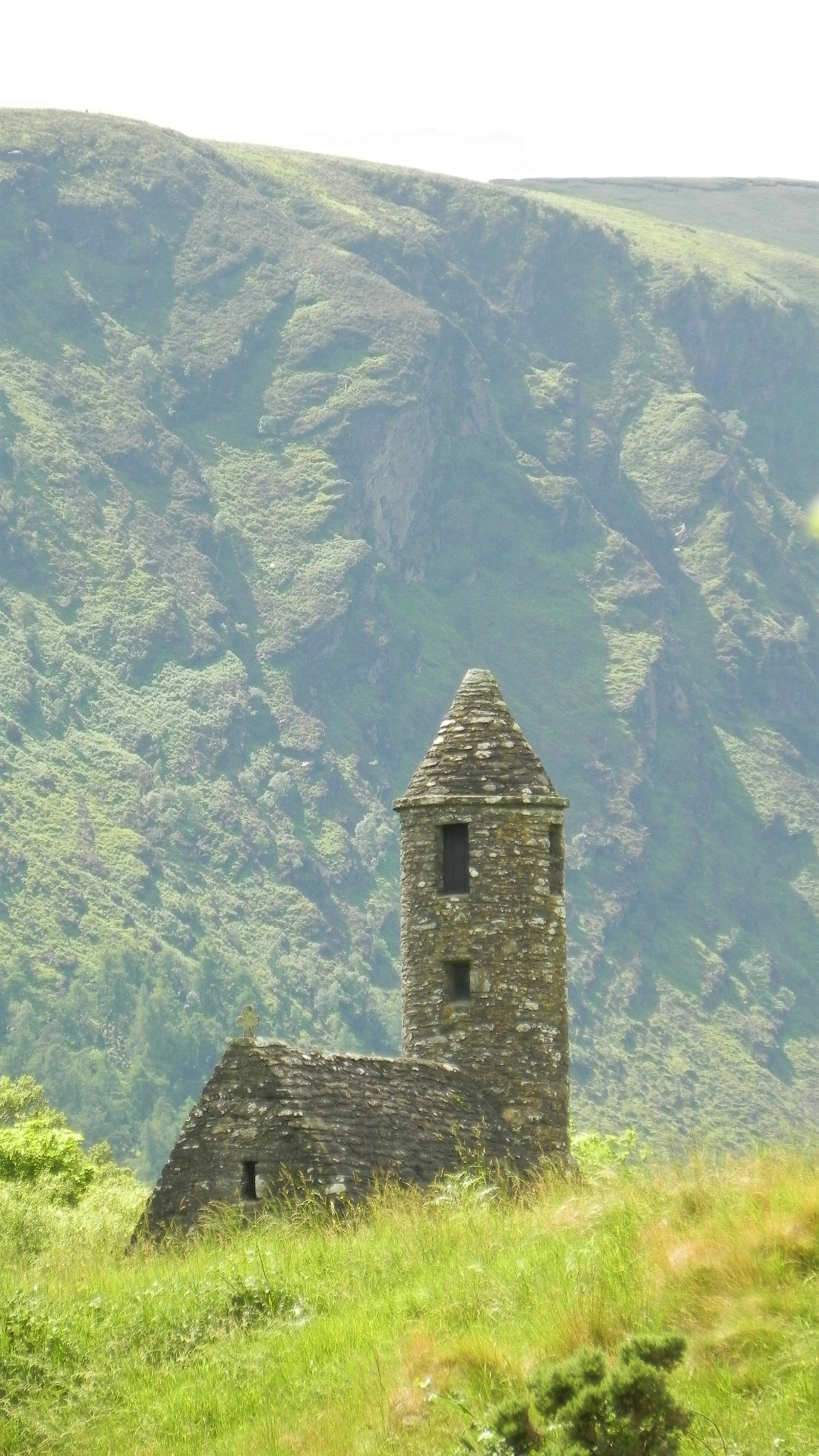 Stone tower ruin in a green, hilly landscape in Glendalough, Ireland.