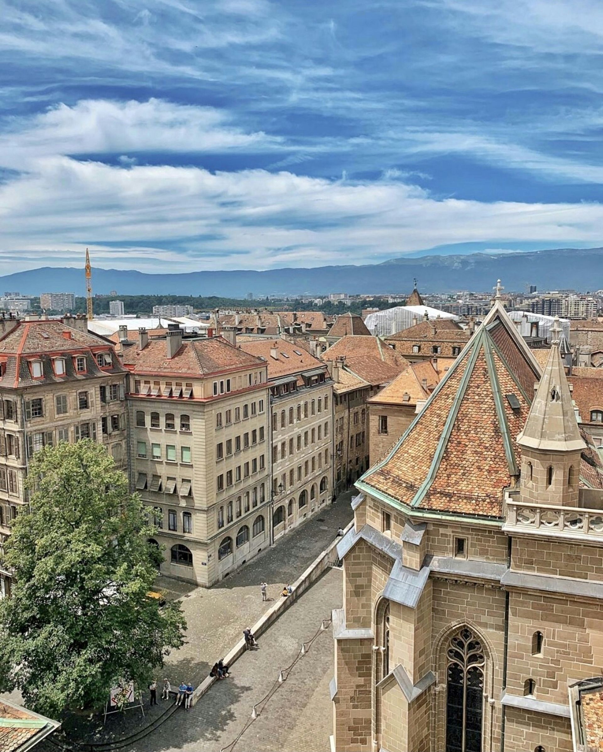 Rooftop view of Geneva, Switzerland, with buildings, a cathedral, and a cloudy blue sky.