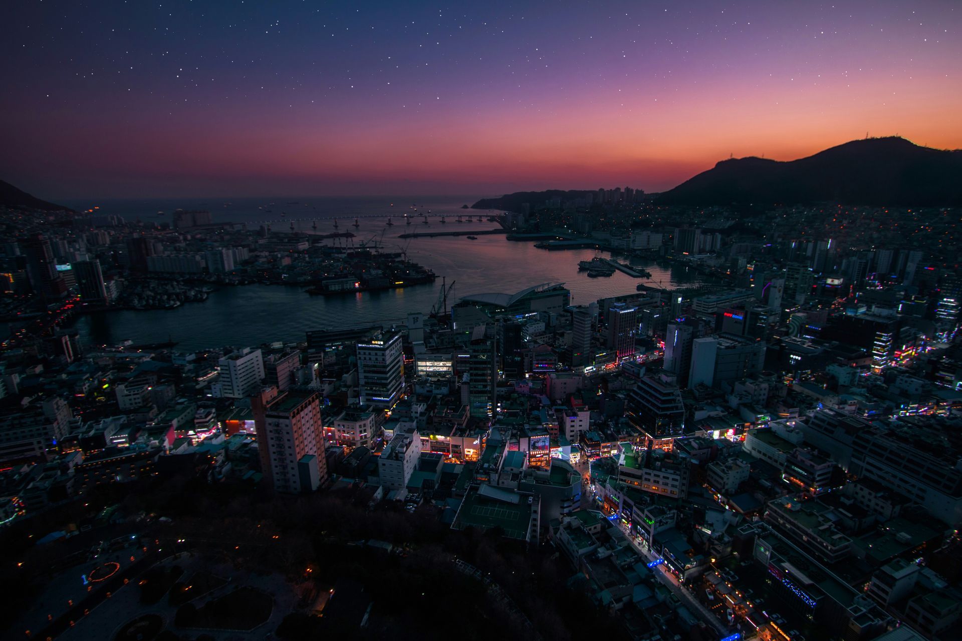 Busan skyline at dusk with lights, water, mountains, and a starry sky in South Korea.