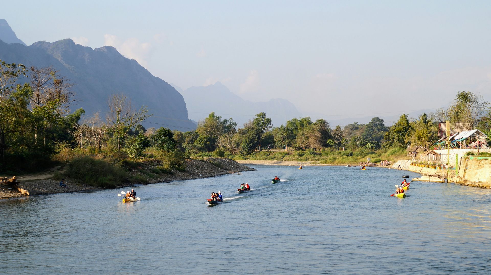 River scene with boats, mountains in the background, sunny day in Vang Vieng, Laos.