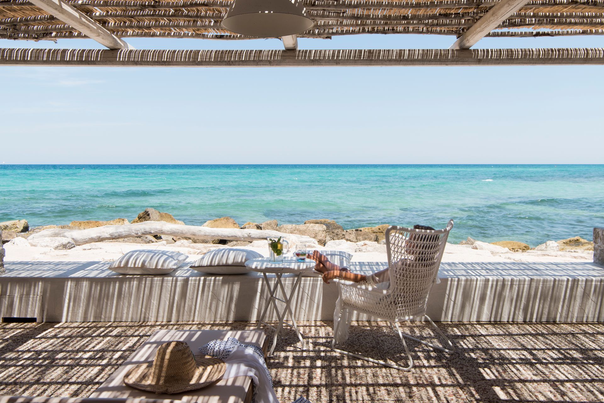 There is a table and chairs on the beach with a view of the ocean at La Peschiera Hotel in Puglia, Italy.