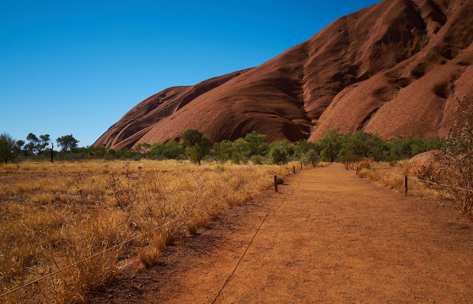 A dirt road in the desert with Uluru Rock in the background in Australia.