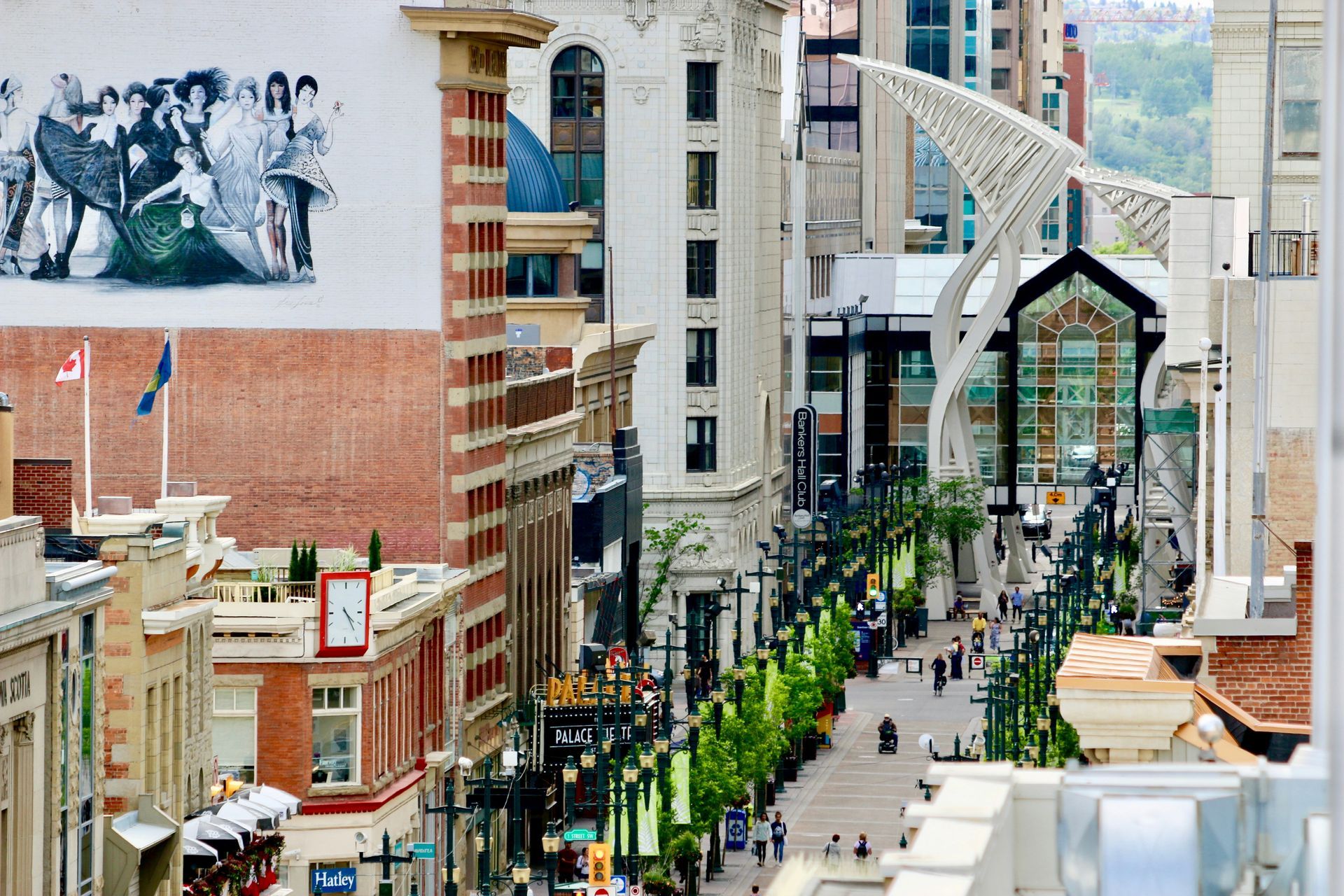 A view of Stephen Avenue Walk in Calgary, Alberta. Tall brick and white buildings line a pedestrian street with art and greenery.