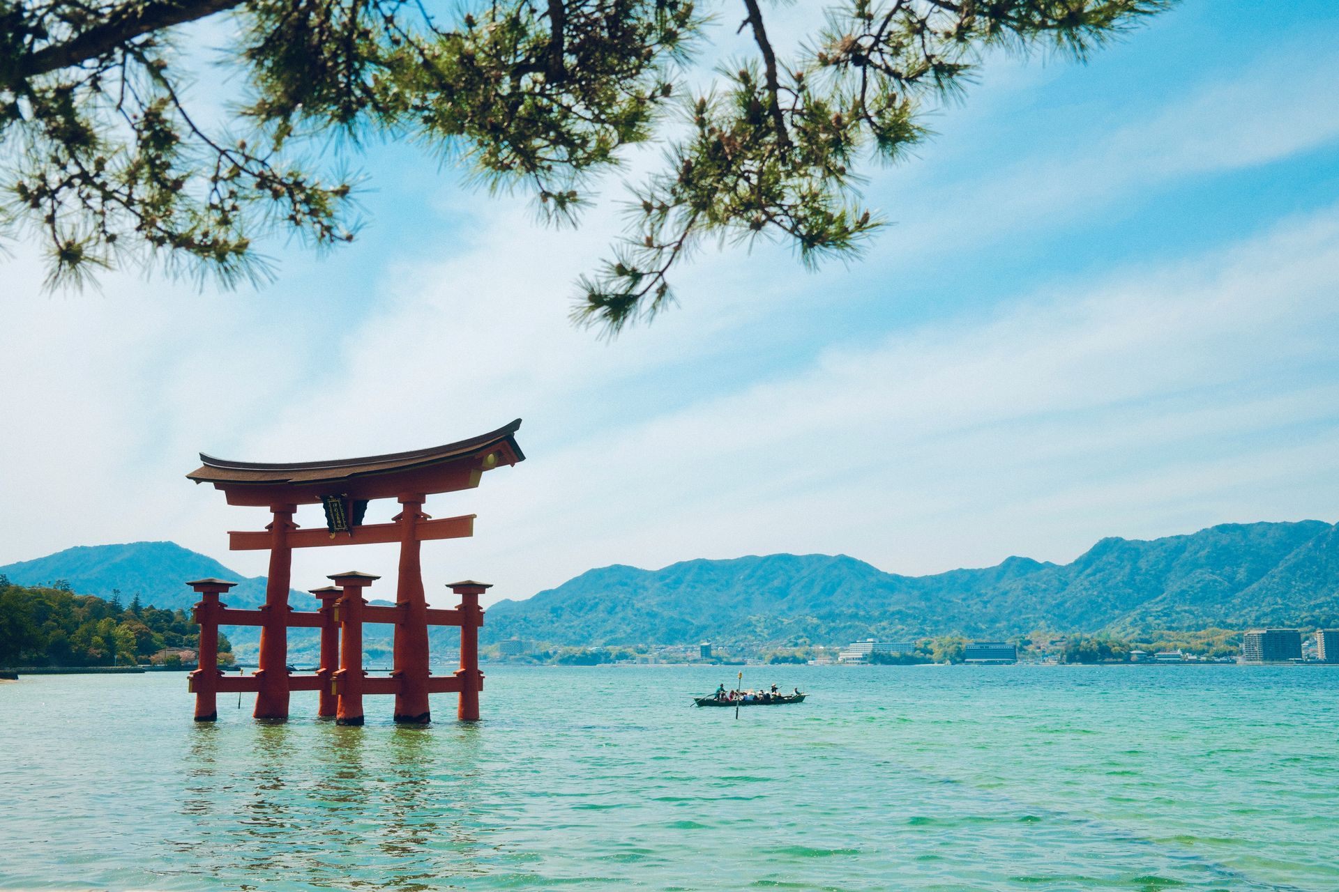 Floating red torii gate in water; blue sky and mountains in the background in Hiroshima, Japan.
