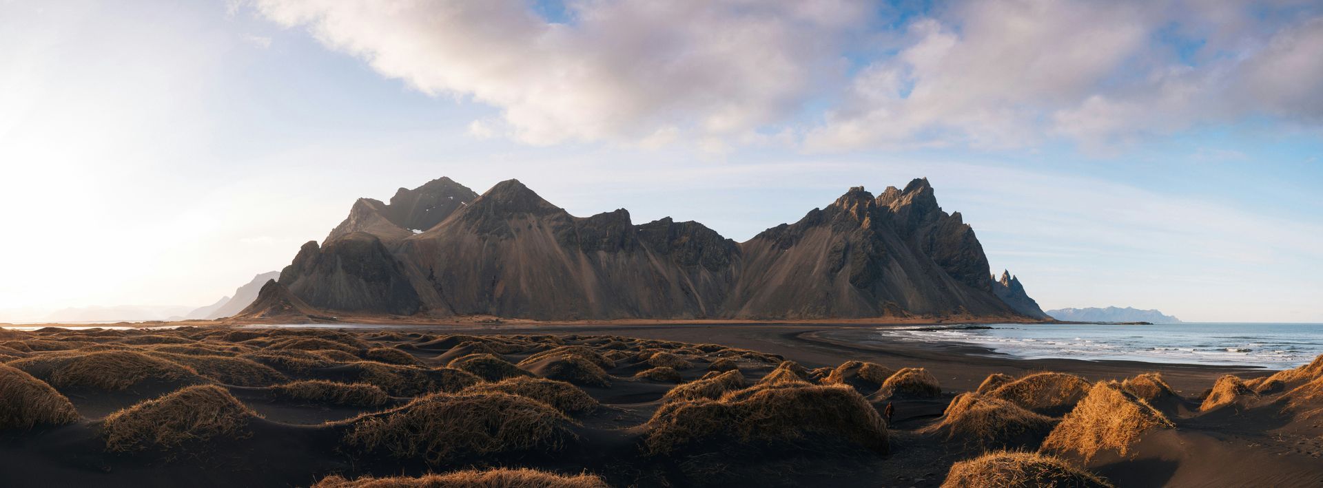 Rocky Mountains overlooking a dark beach and ocean under a cloudy sky in Stokksnes, Iceland.