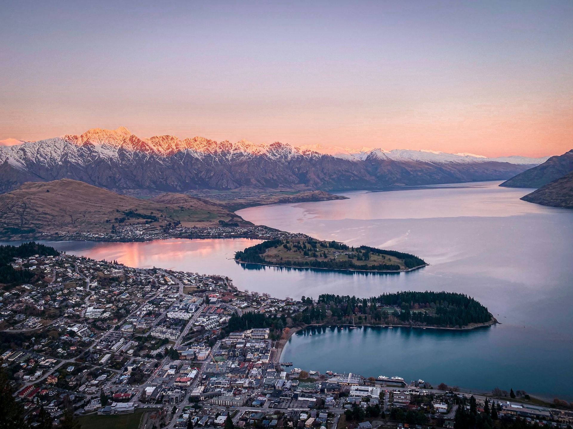 An aerial view of Queenstown, New Zealand, and a lake with mountains in the background.