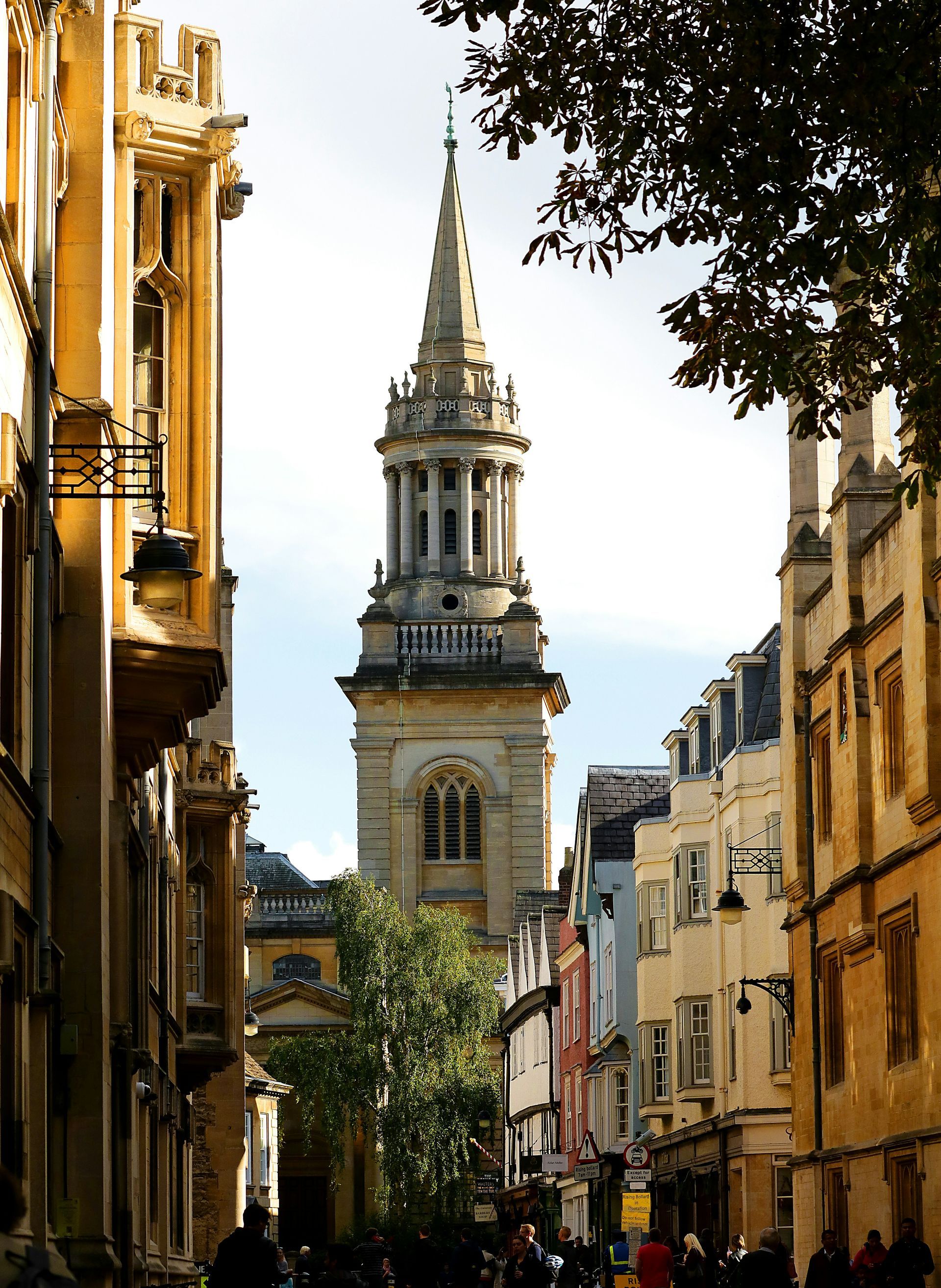 Narrow street lined with buildings, leading to a tall church spire in Oxford, England.