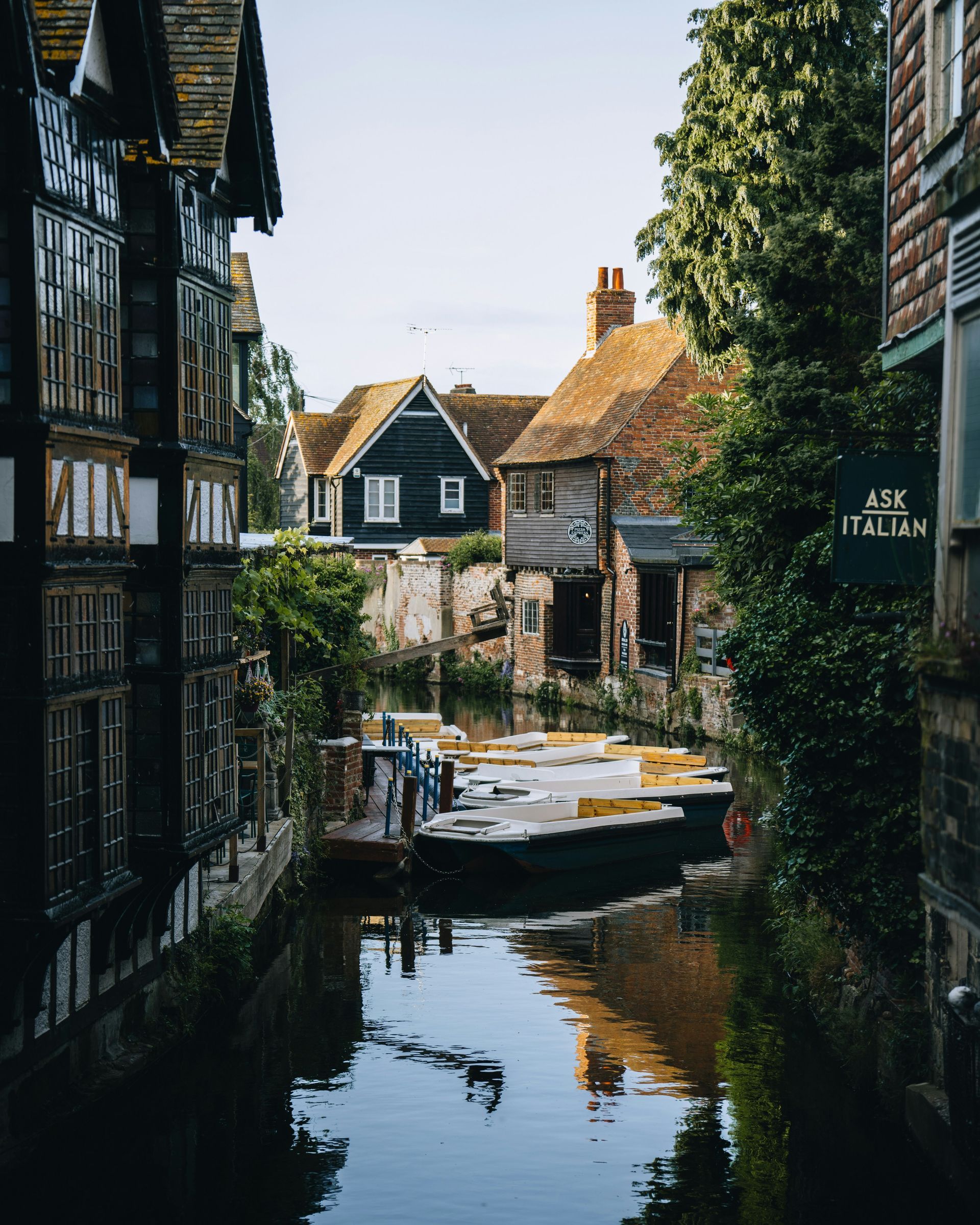 Canal lined with historic buildings and boats, trees, and sky in Canterbury, England.