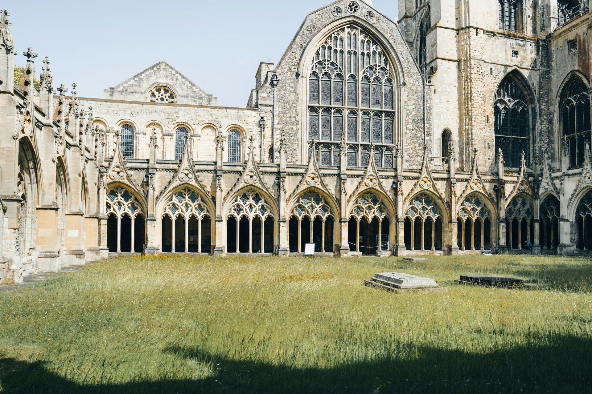 Stone cloister with arches, a grassy courtyard, and a large church building in Canterbury, England.