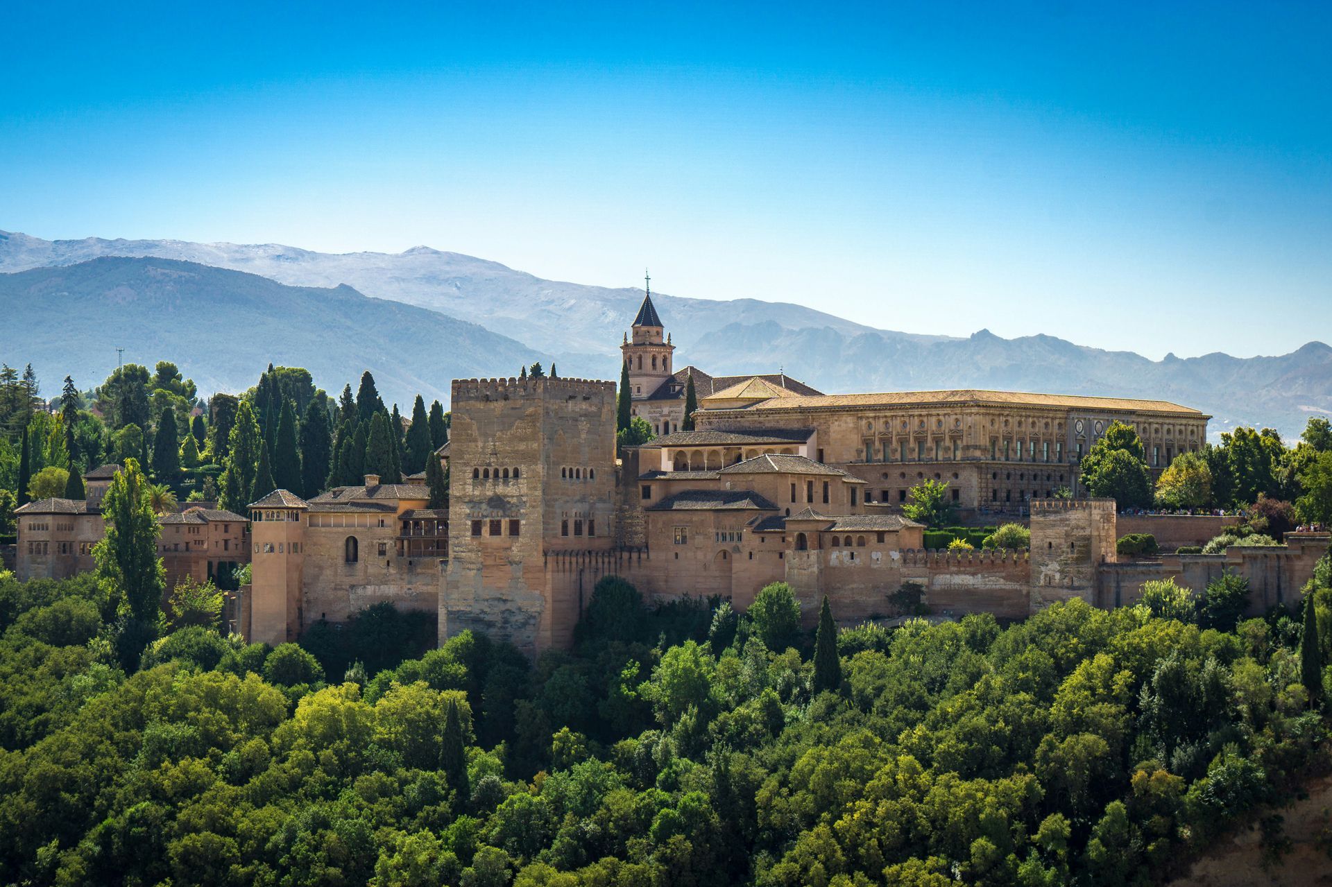 Alhambra palace complex in Granada, Spain, atop a green hillside, under a blue sky.