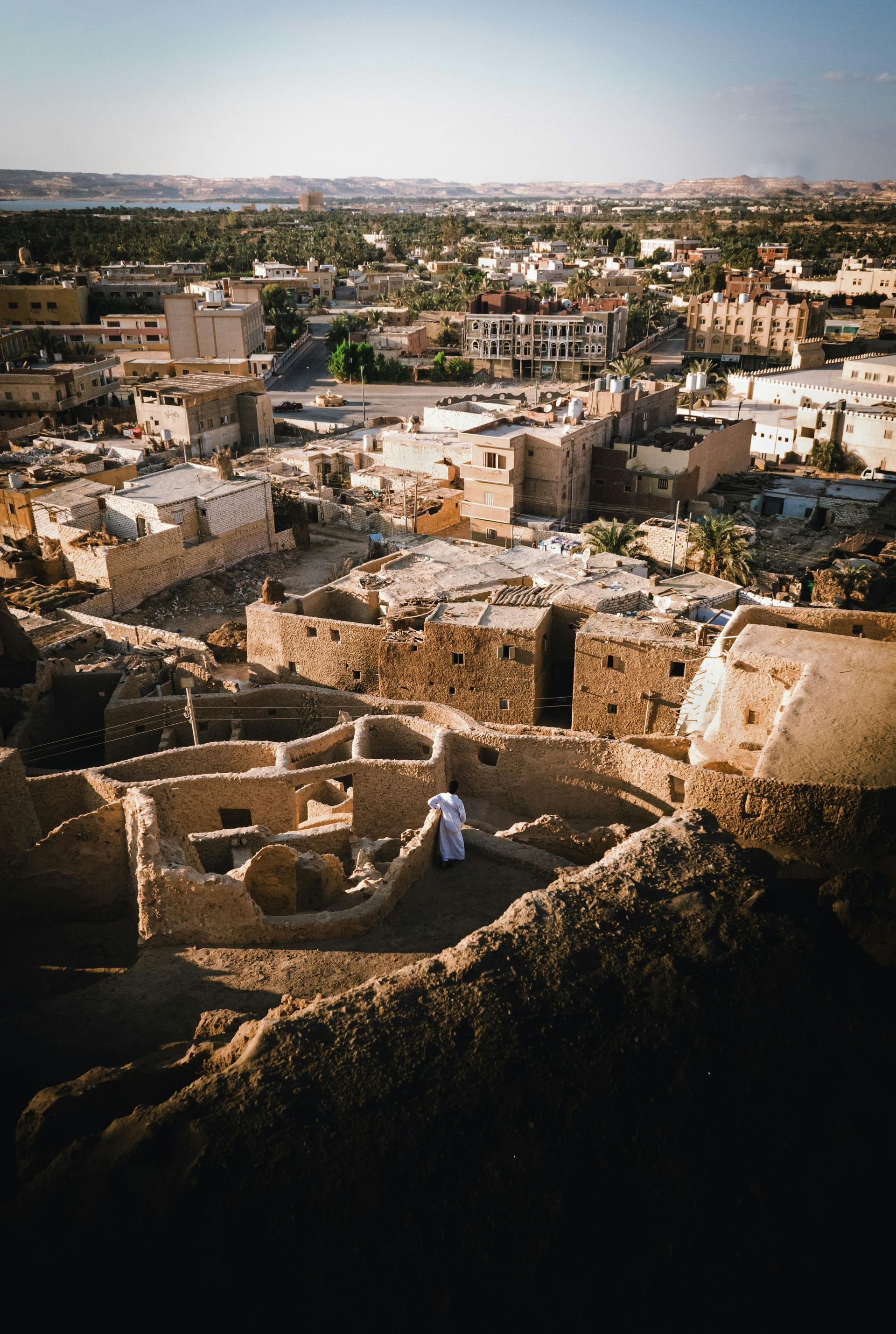 A man is standing on top of a hill overlooking a city in Siwa, Egypt.