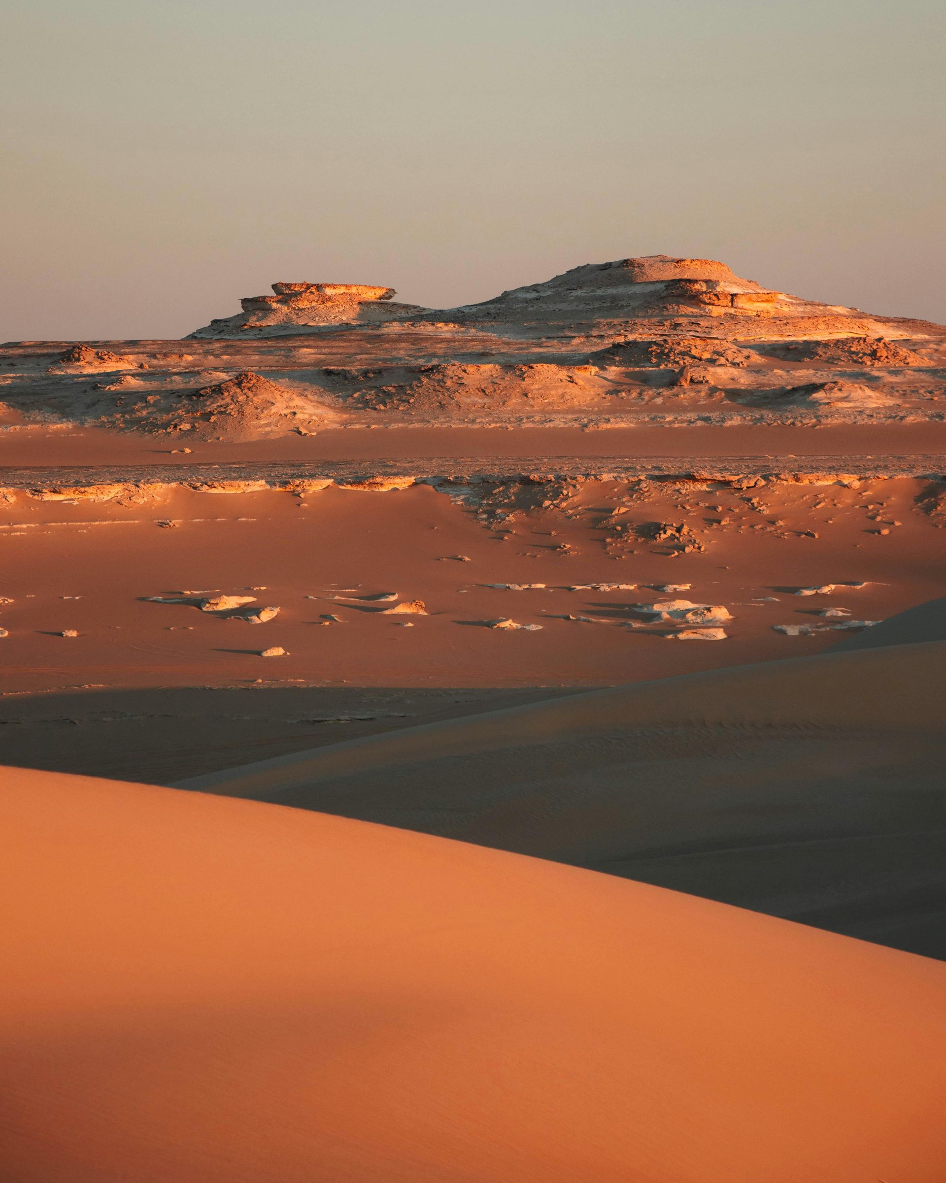 A large sand dune in the middle of a desert with mountains in the background in Siwa, Egypt.