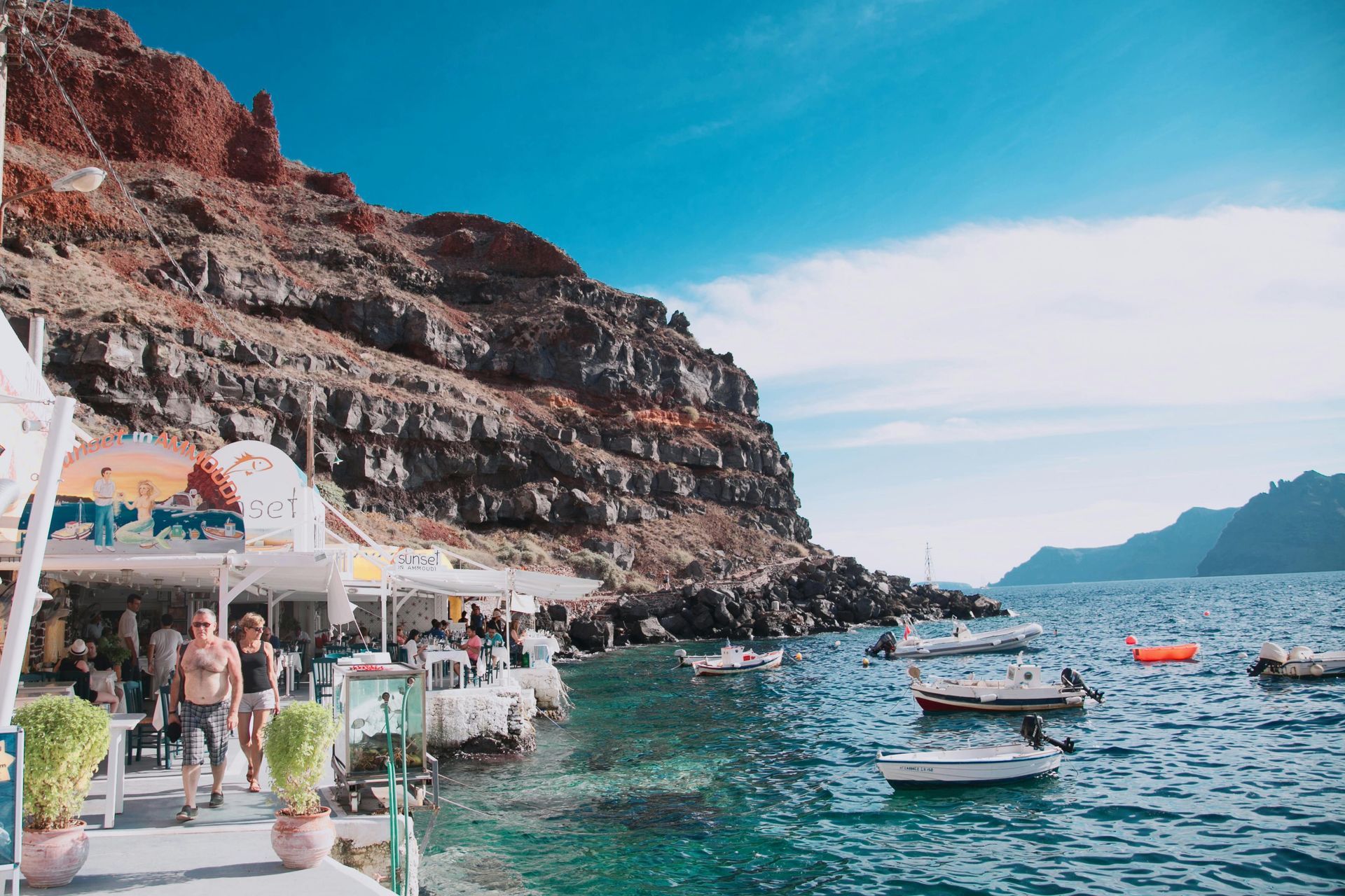 A couple of people walking down a pier next to a body of water in Santorini, Greece.