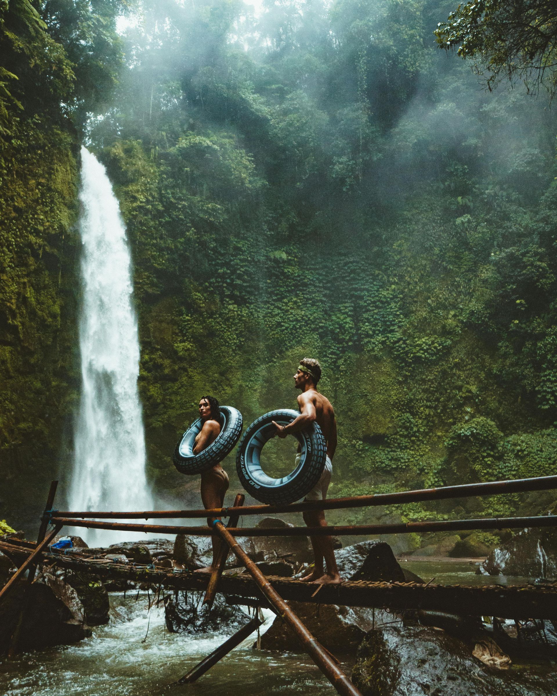 A man and a woman are standing on a bridge in front of a waterfall in Indonesia.