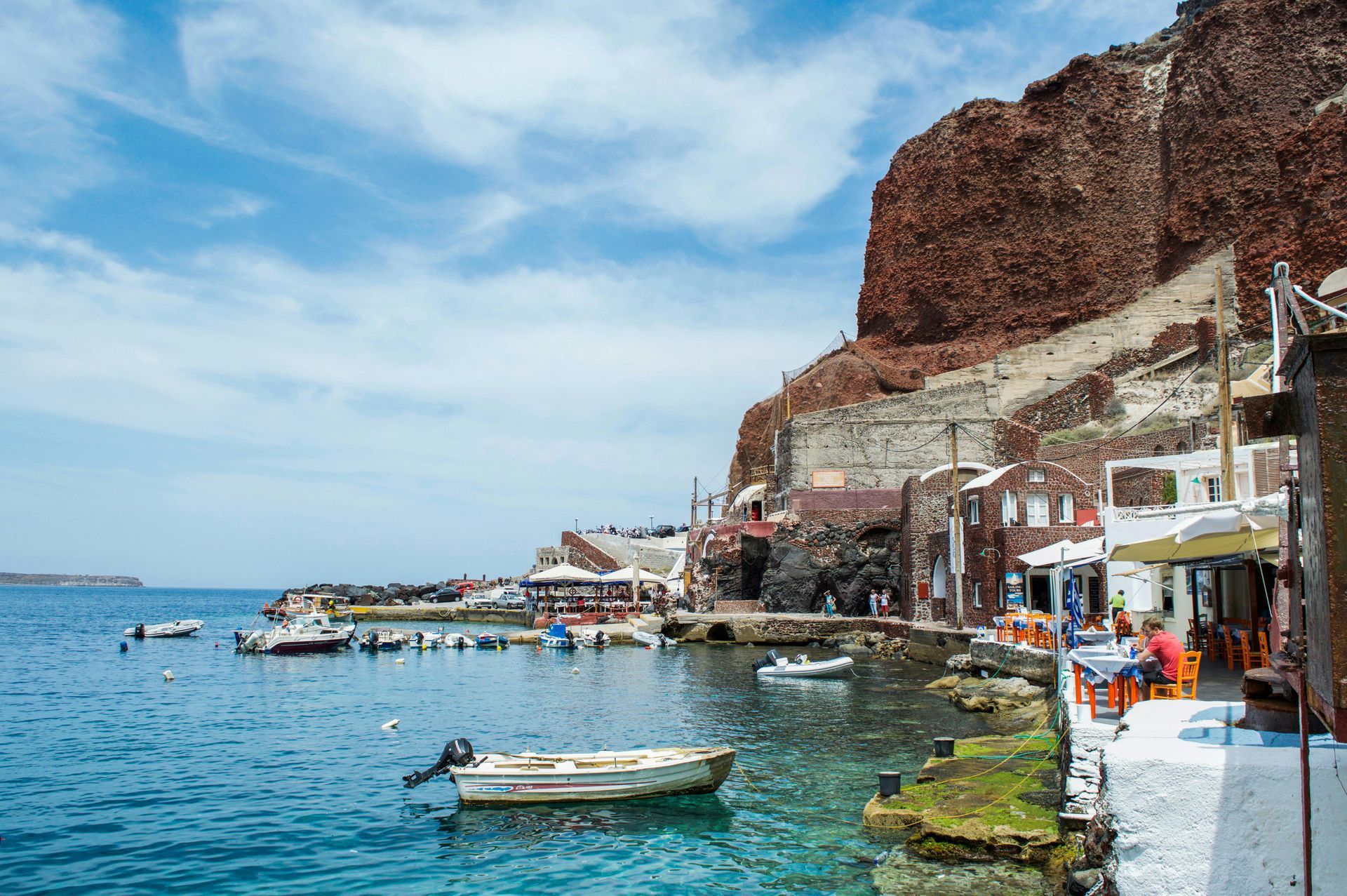 A boat is docked in the water near a cliff in Santorini, Greece.