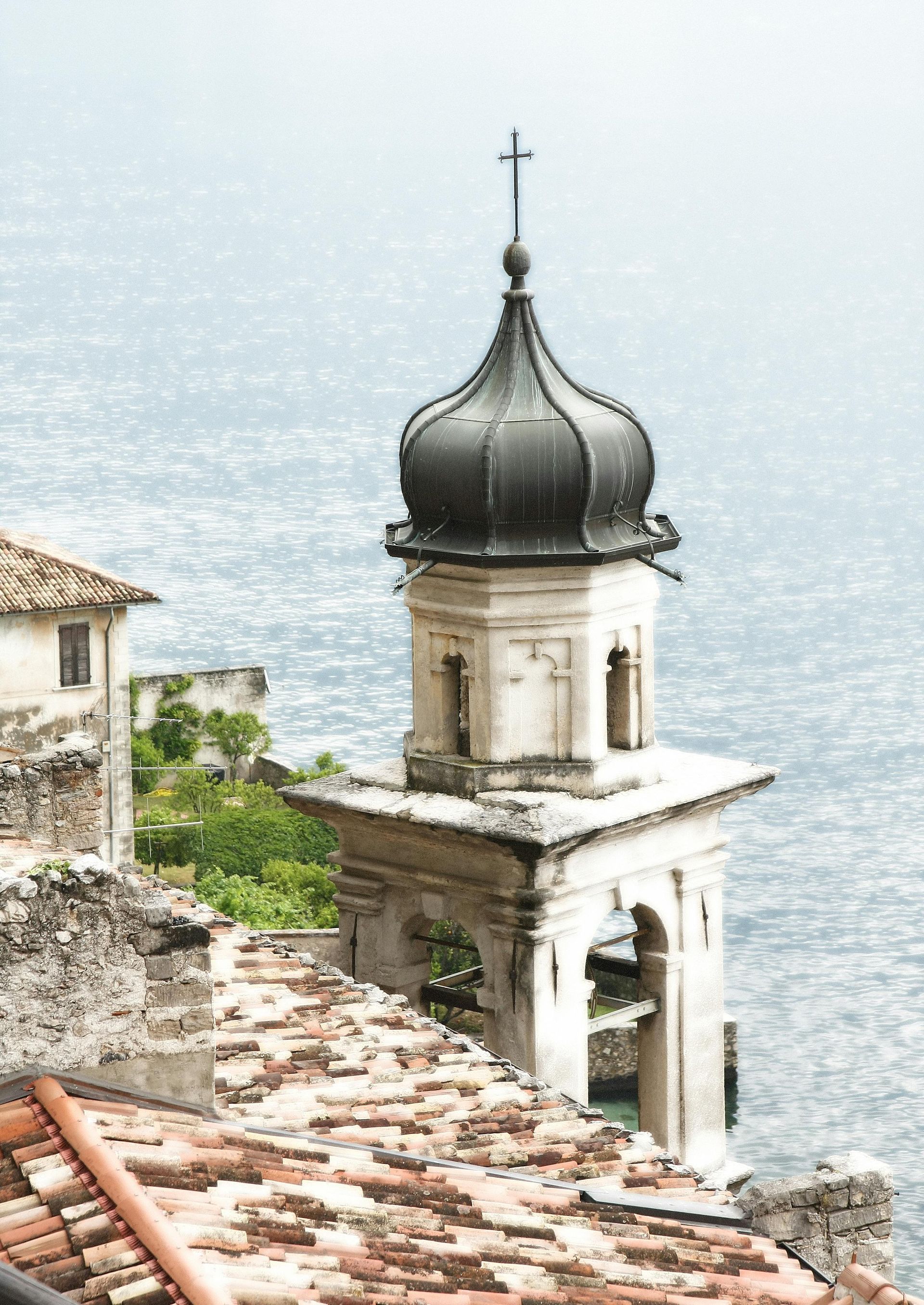 A bell tower with a cross on top of it on Lake Garda, Italy.