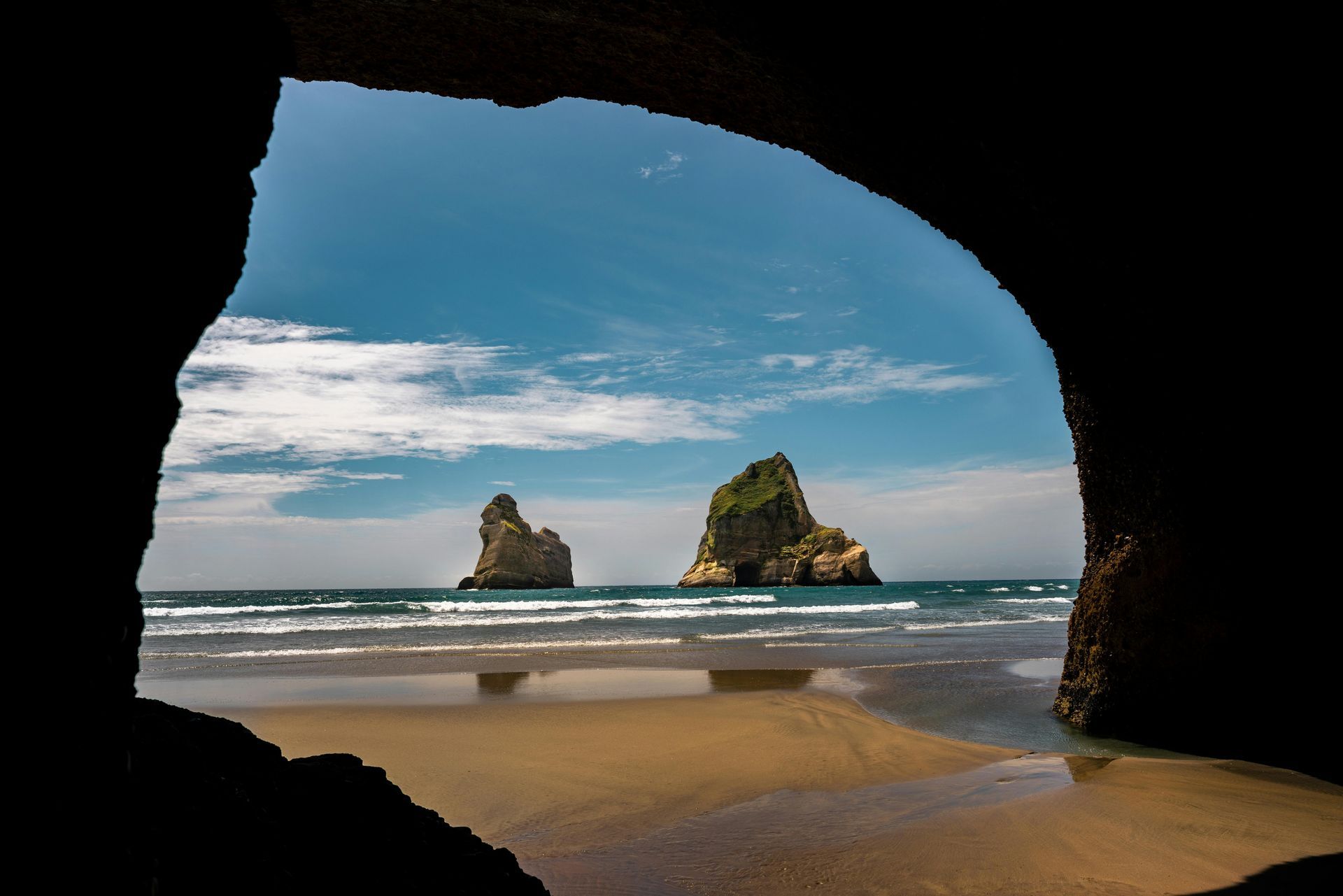 A view of a beach from a cave with rocks in the background in New Zeland.