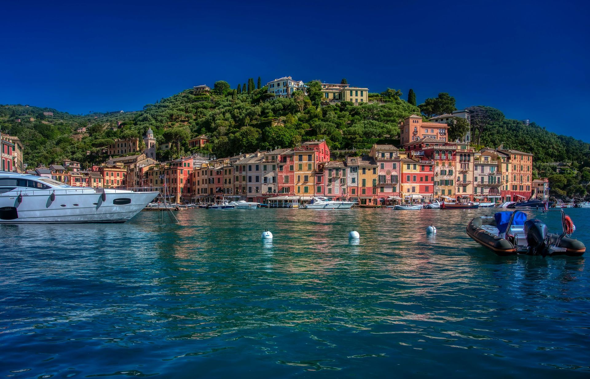 A group of boats are docked in a harbor with Portofino, Italy in the background.