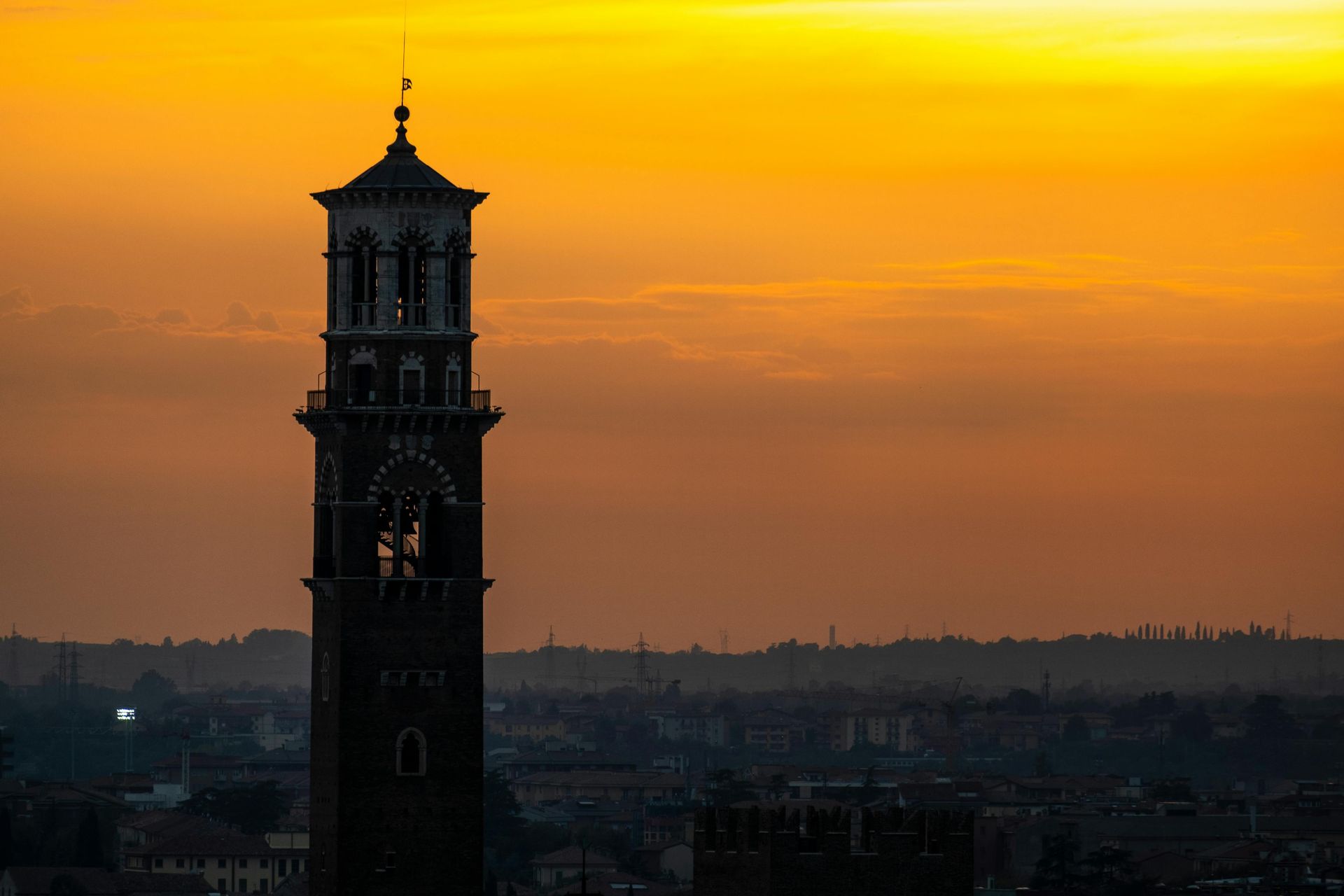 A clock tower is silhouetted against a sunset sky in Verona, Italy.