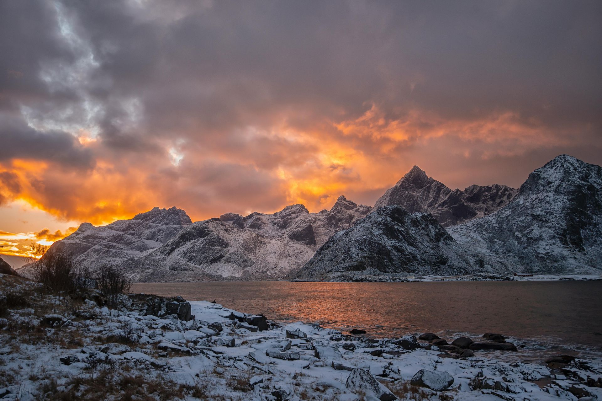 A sunset over a snowy mountain range with a lake in the foreground  on the Norwegian Coast.