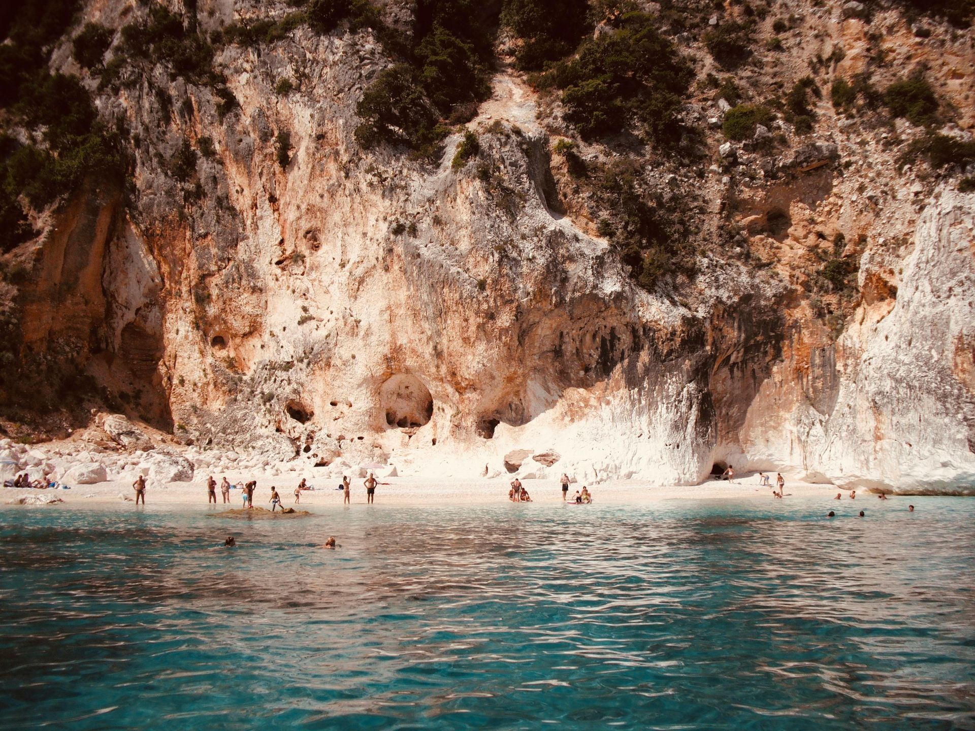 A group of people are swimming in the ocean near a beach in Sardinia, Italy.