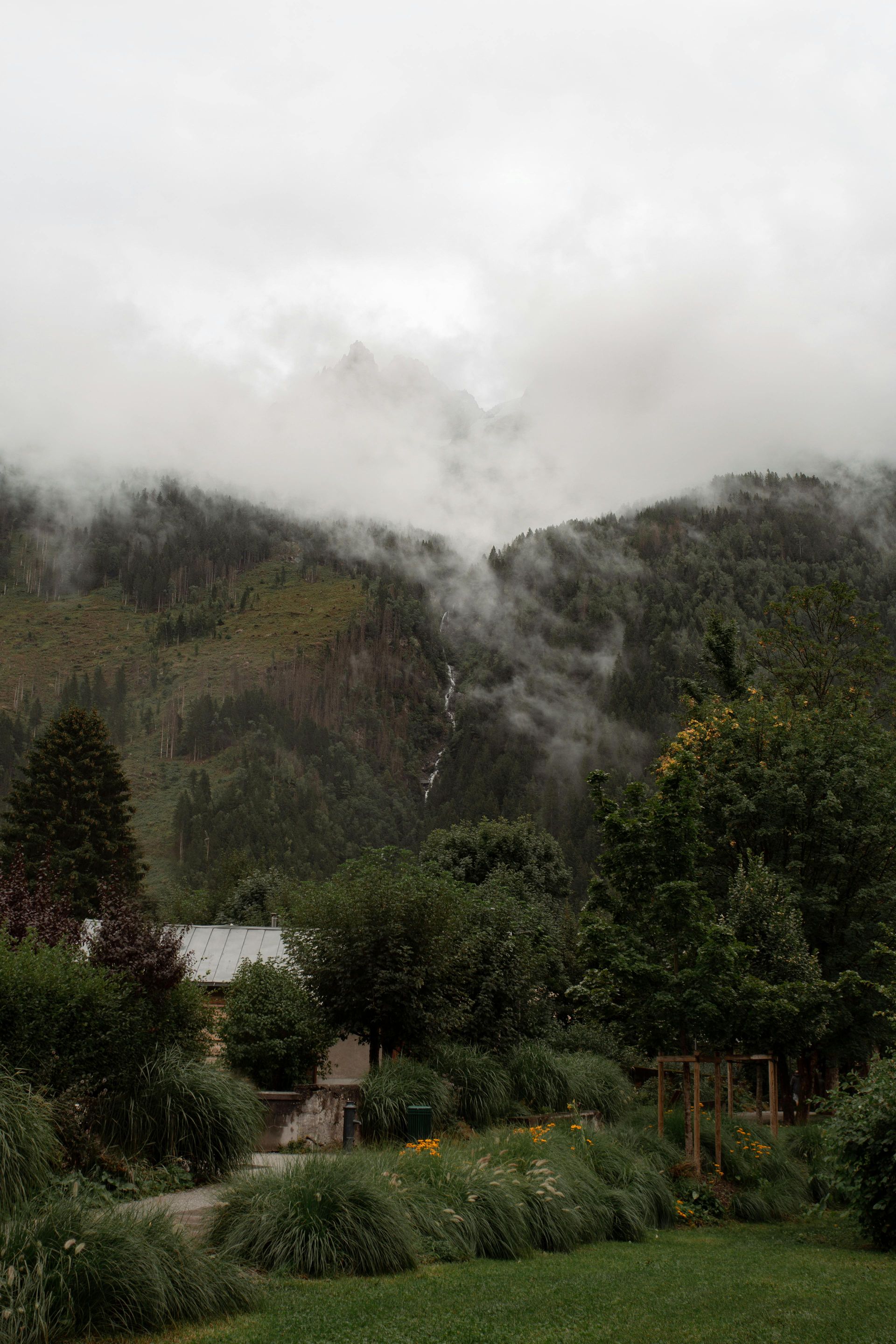 A house in the middle of a forest with mountains in the background covered in fog in Chamonix, France.