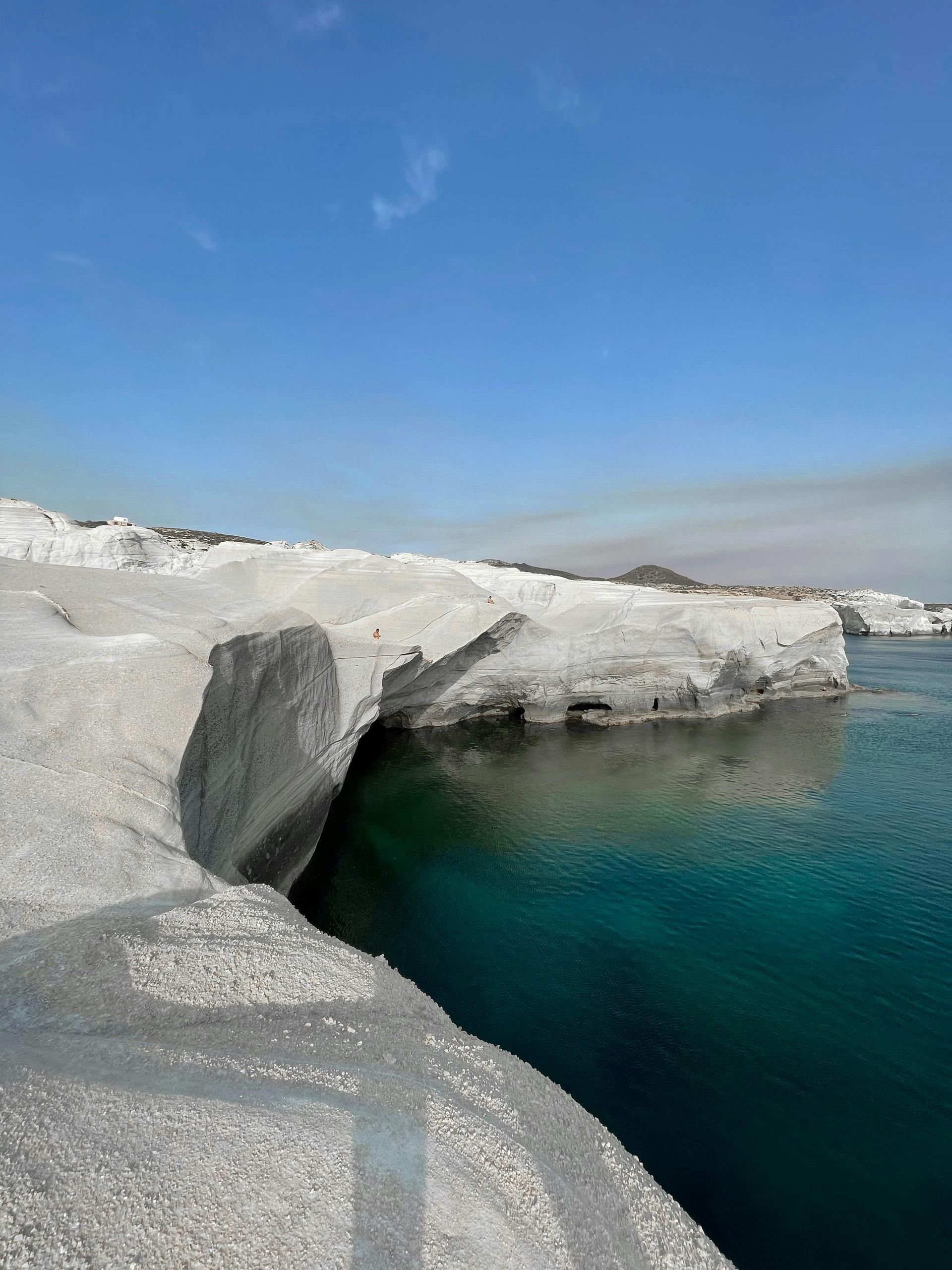 A large rock is sitting on the edge of a body of water on Sarakiniko Beach in Milos, Greece.