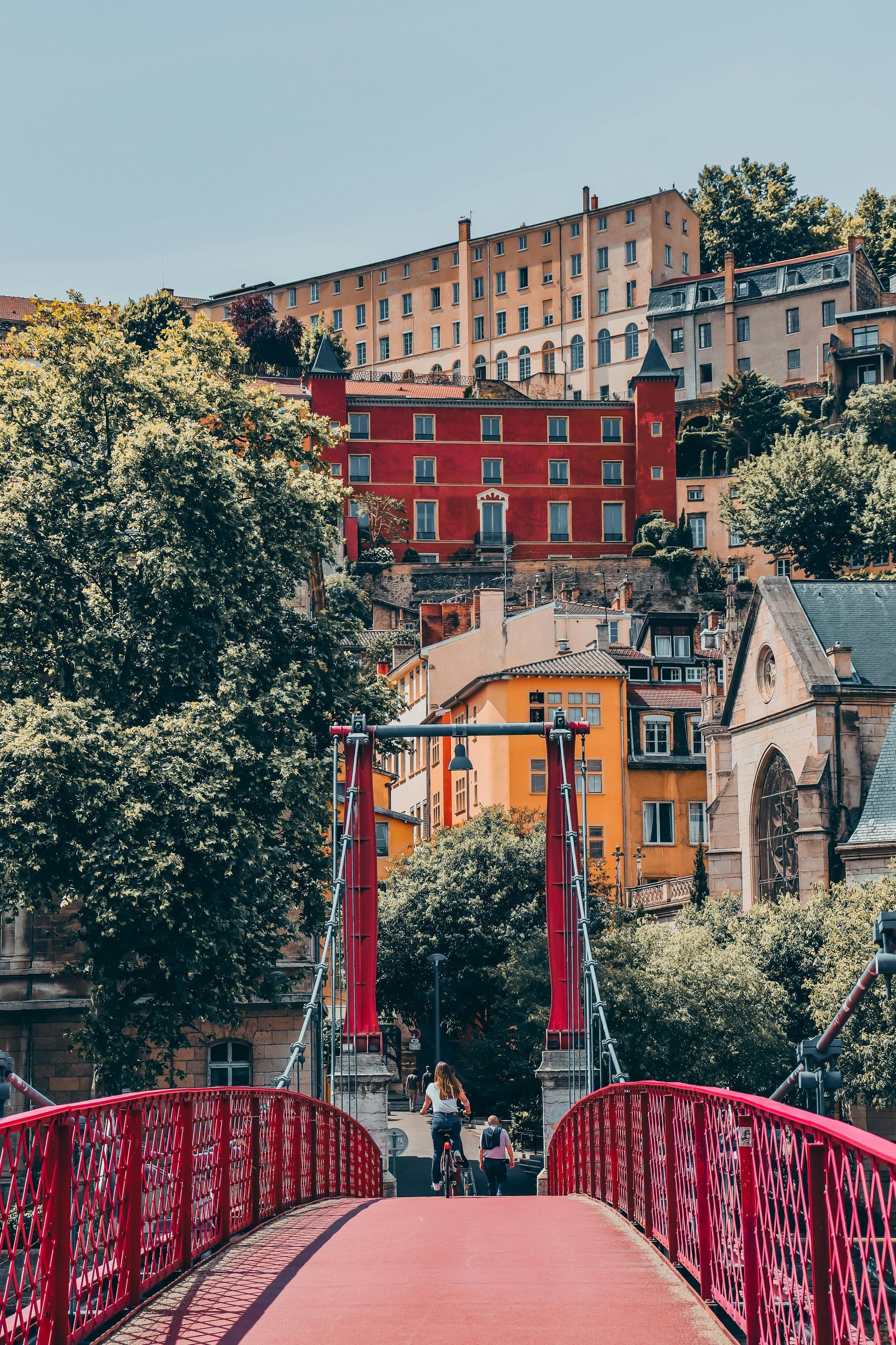 A red bridge leading to a city with buildings in the background in Lyon, France.