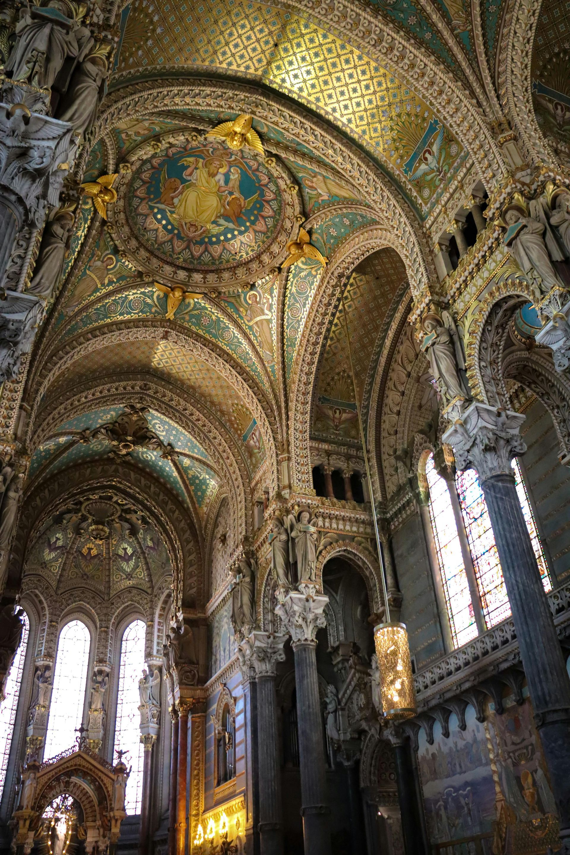 The inside of a church with a very ornate ceiling and stained glass windows in Lyon, France.