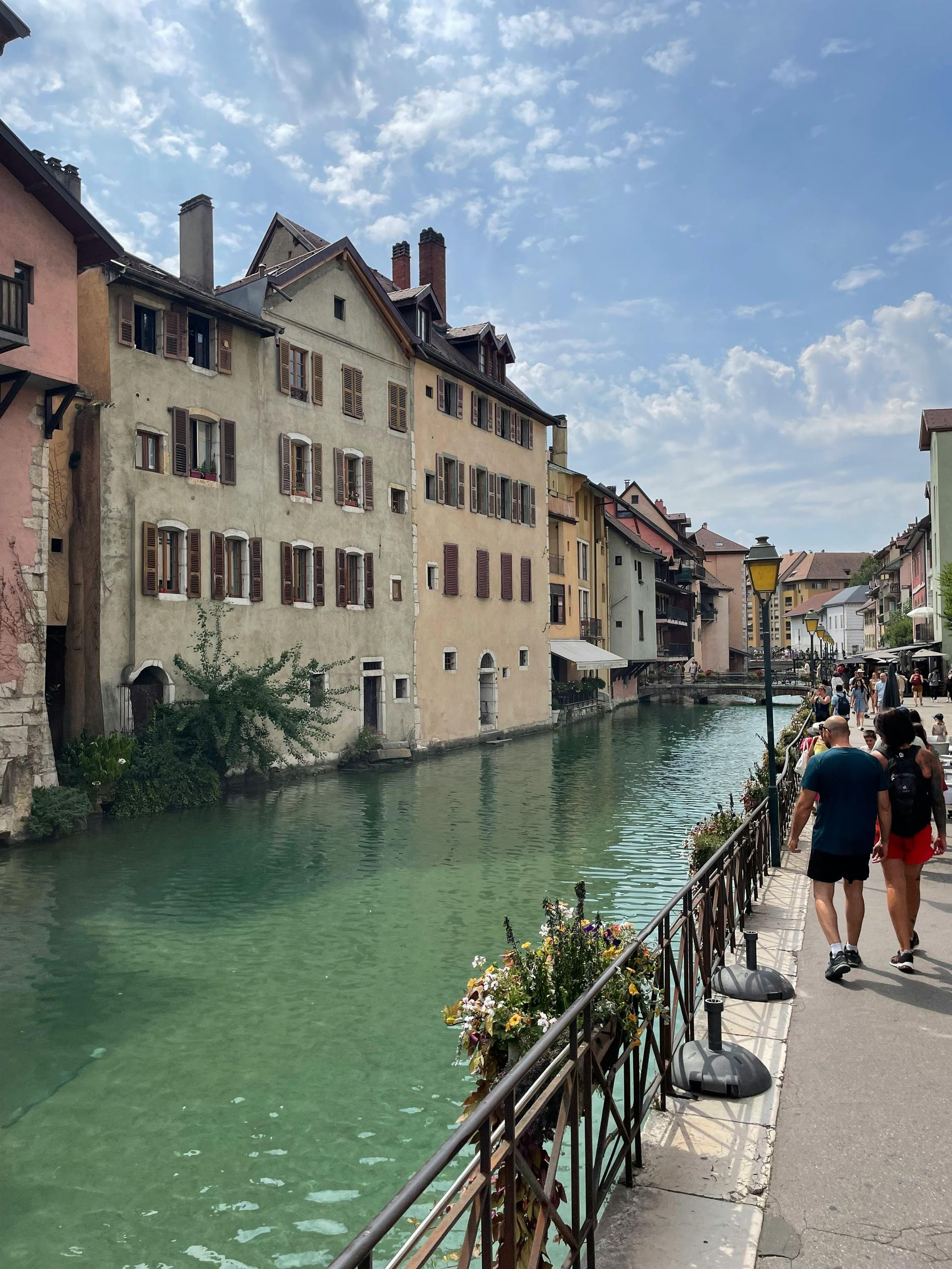 A couple walking down a sidewalk next to a river in Annecy, France.