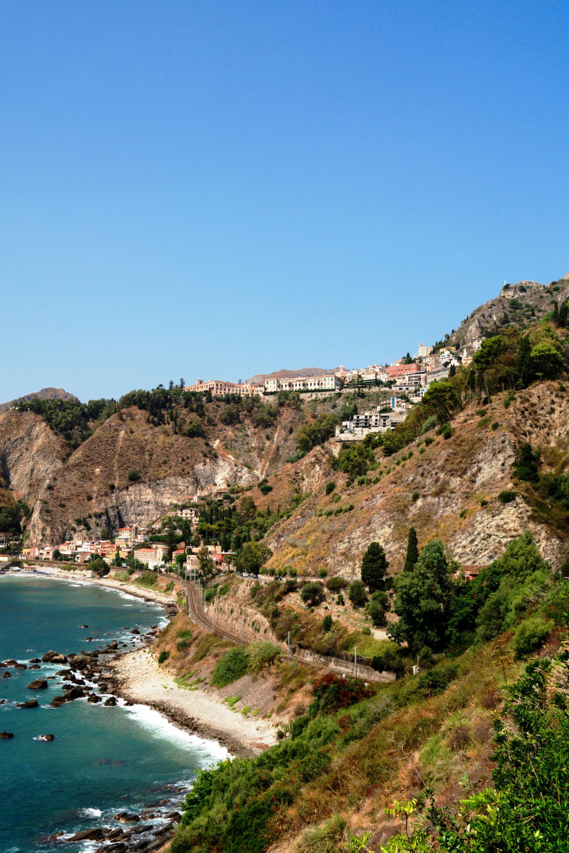 A cliff overlooking a body of water with a city in the background in Sicily, Italy.