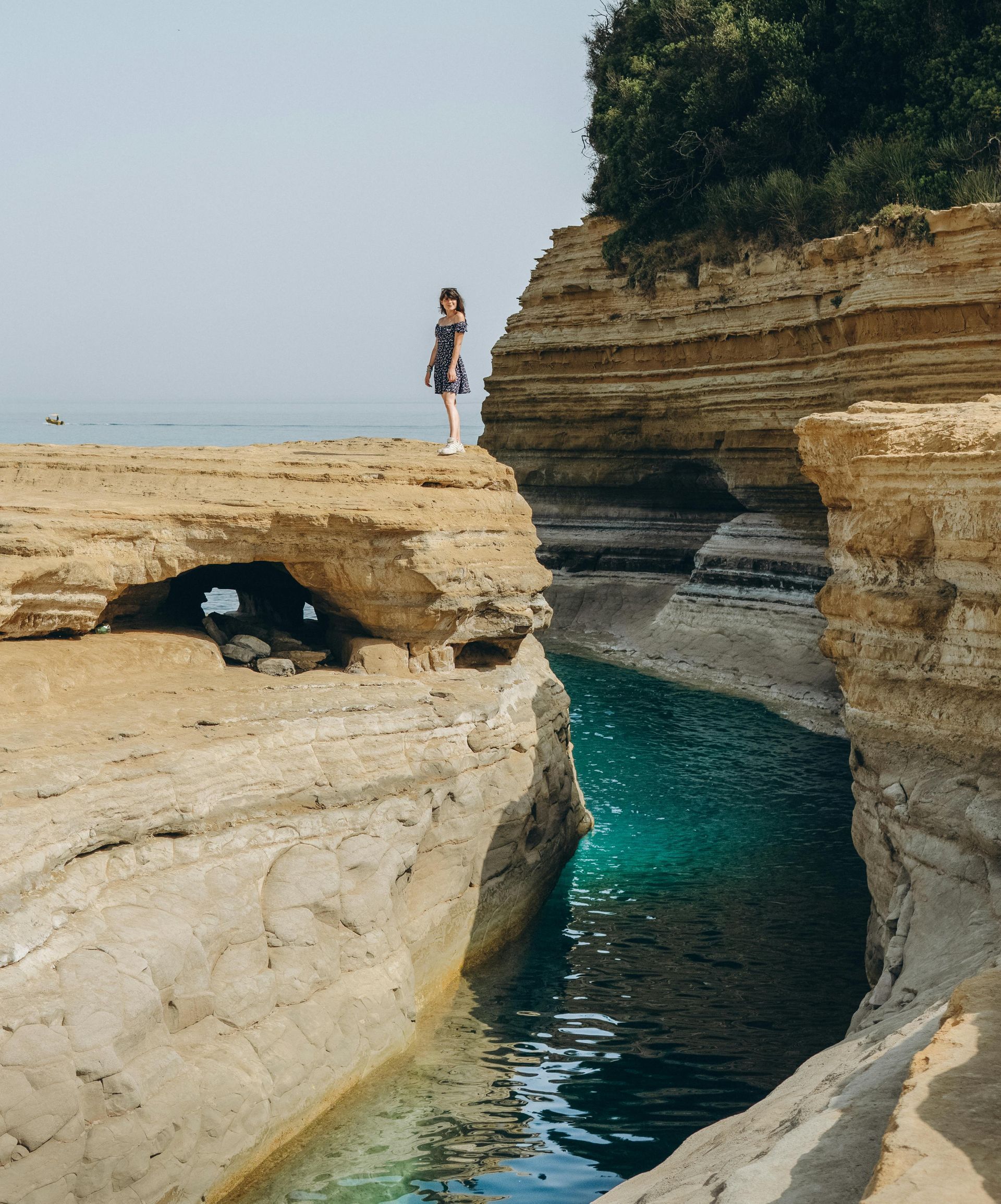 A woman is standing on a cliff overlooking a body of water in Corfu, Greece.