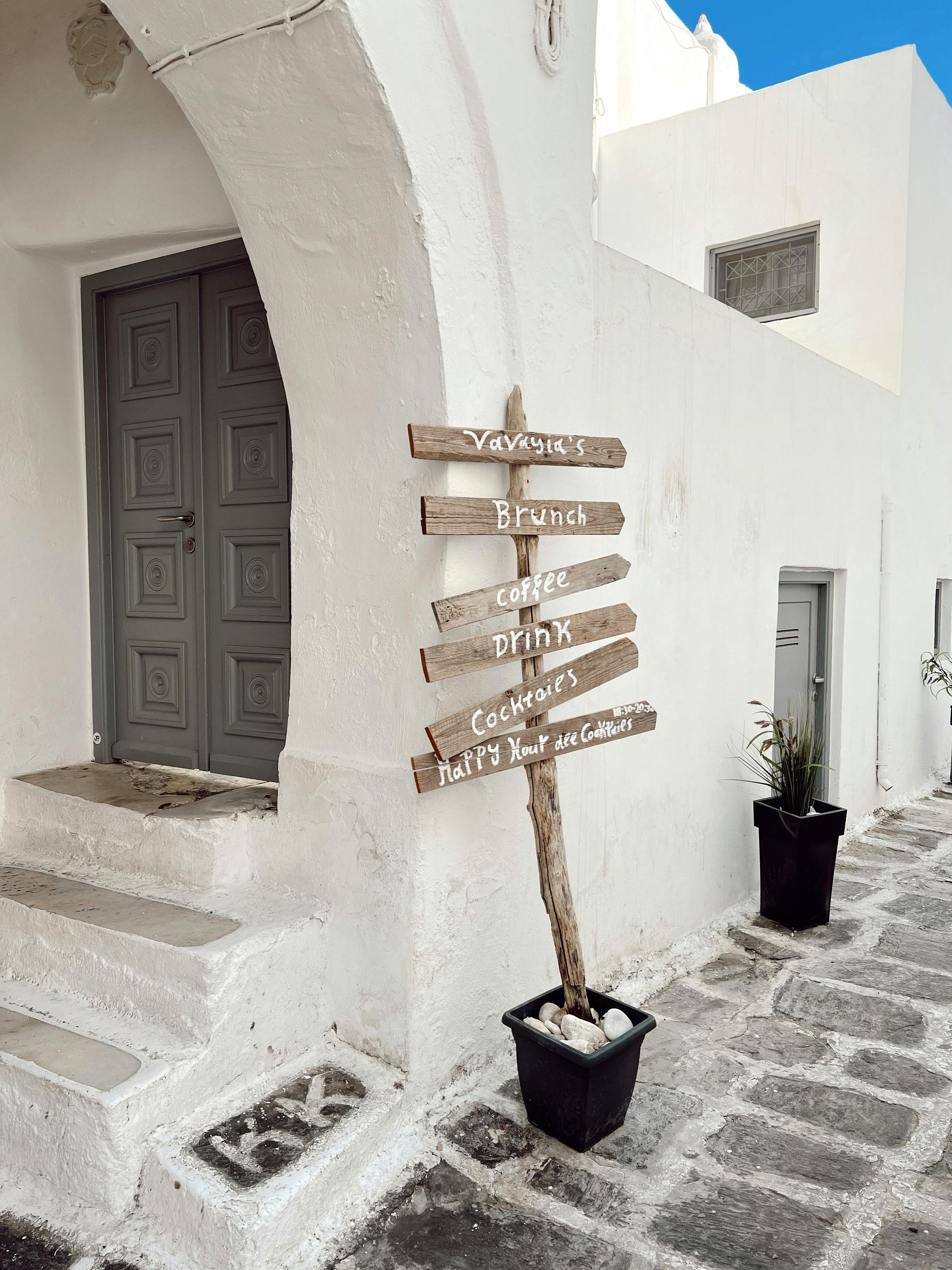 A white building with a wooden sign on the side of it in Paros, Greece.