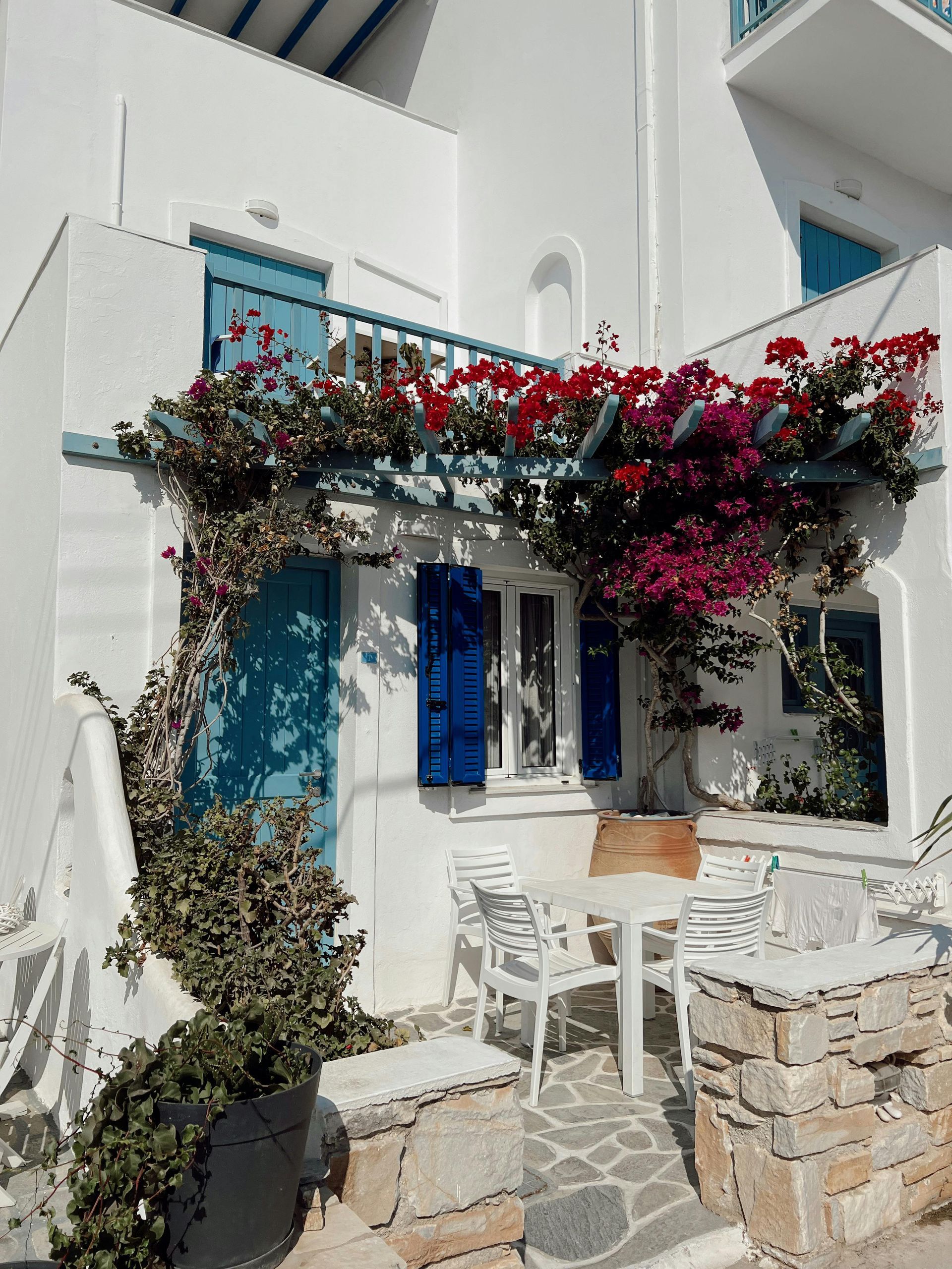 A white building with blue shutters and flowers on it in Paros, Greece.