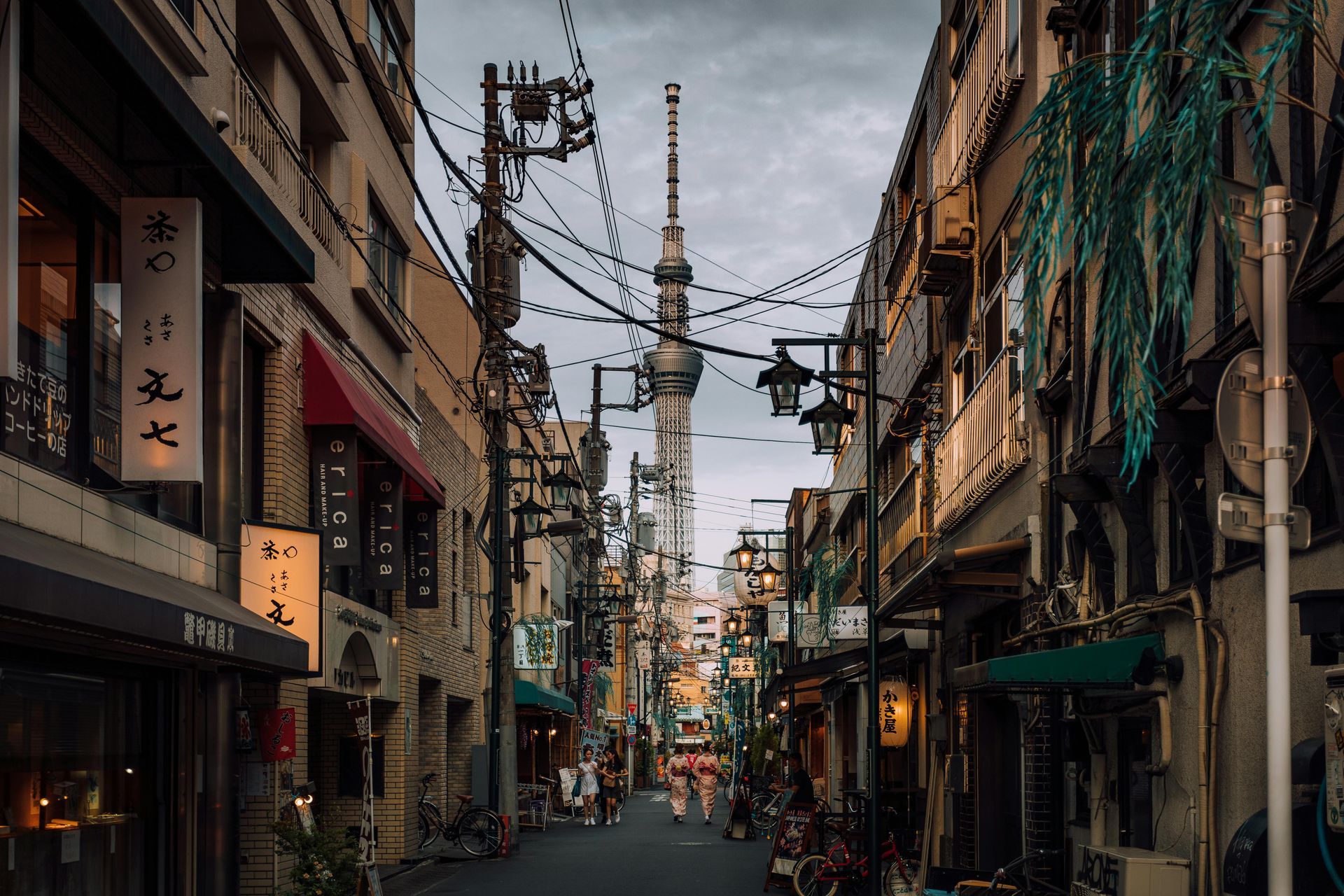 A narrow street in a city with a tower in the background in Japan.