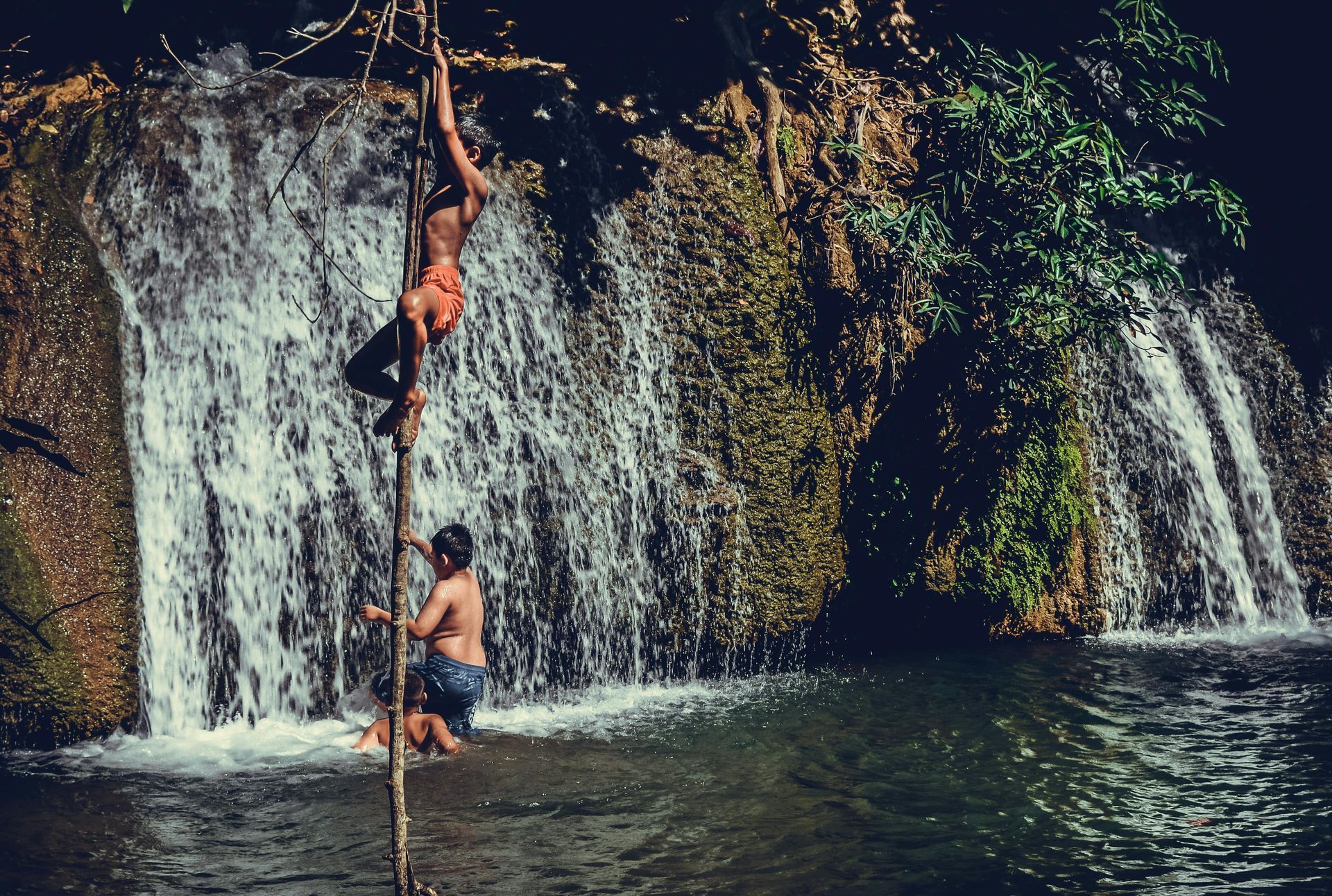 Two men are playing in the water near a waterfall in Thailand.