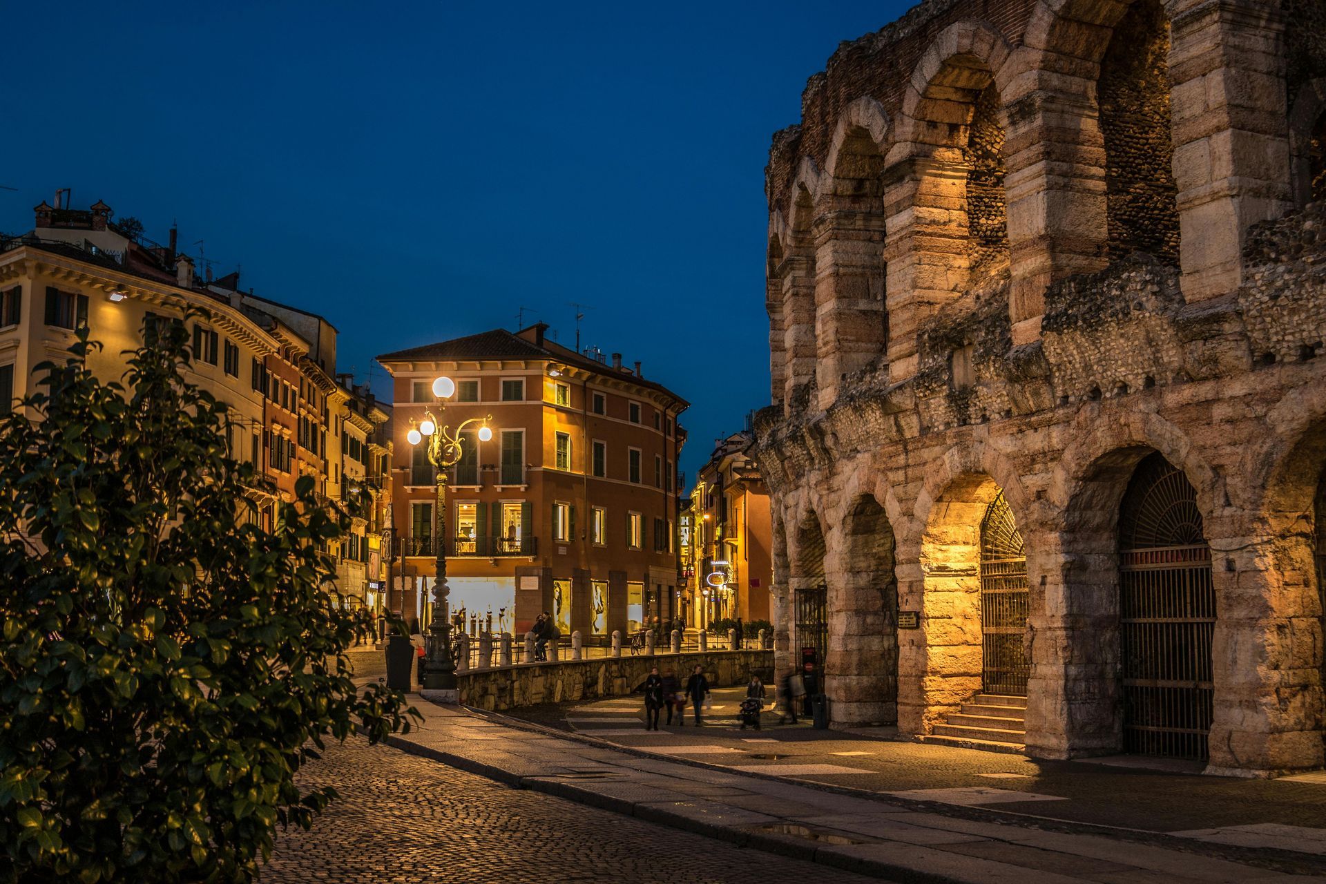 A group of people are standing in front of an ancient building at night in Verona, Italy.