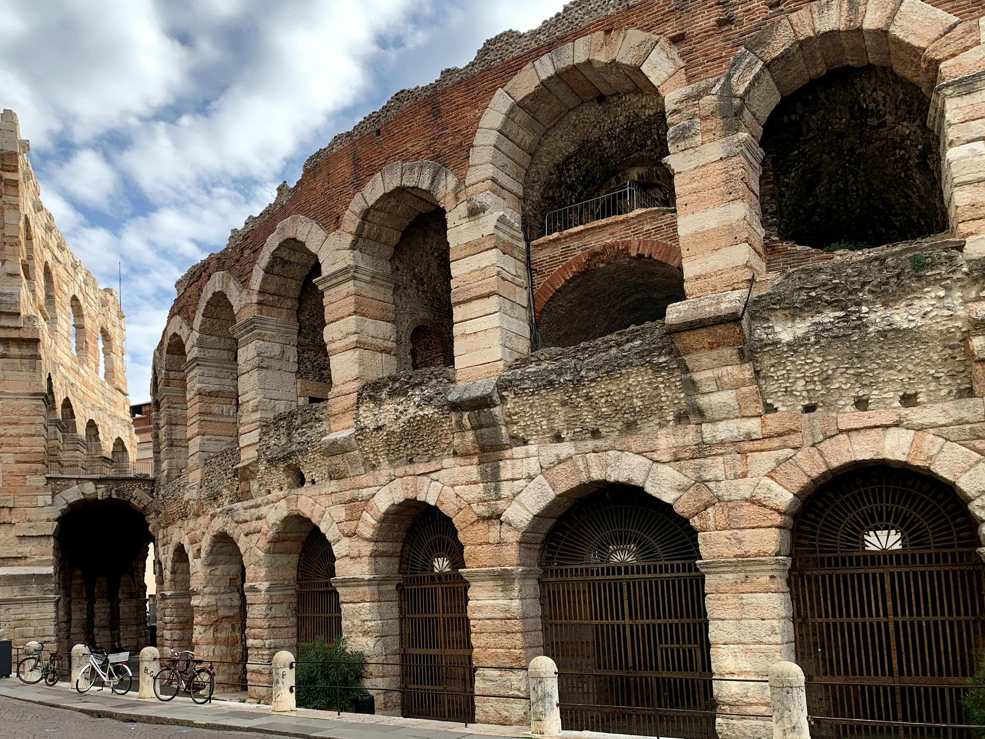 A large stone building with arches and a fence in front of it in Verona, Italy.