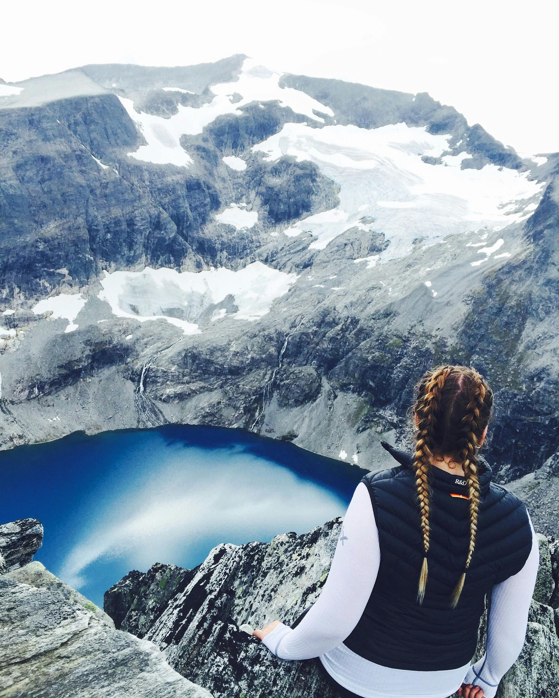 A woman sitting on top of a mountain looking at a lake in Norway.