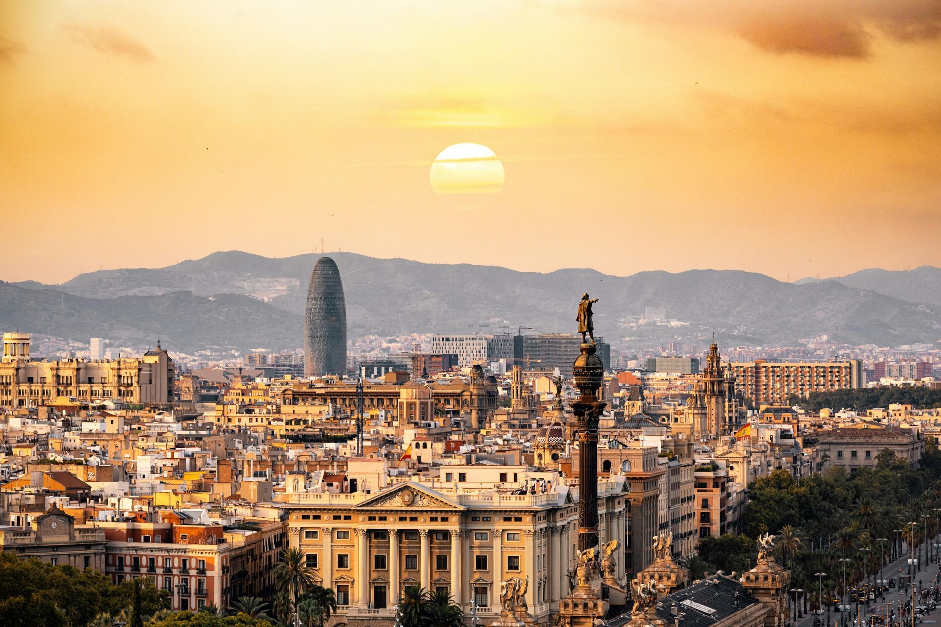 The sun is setting over a city with a statue in the foreground.