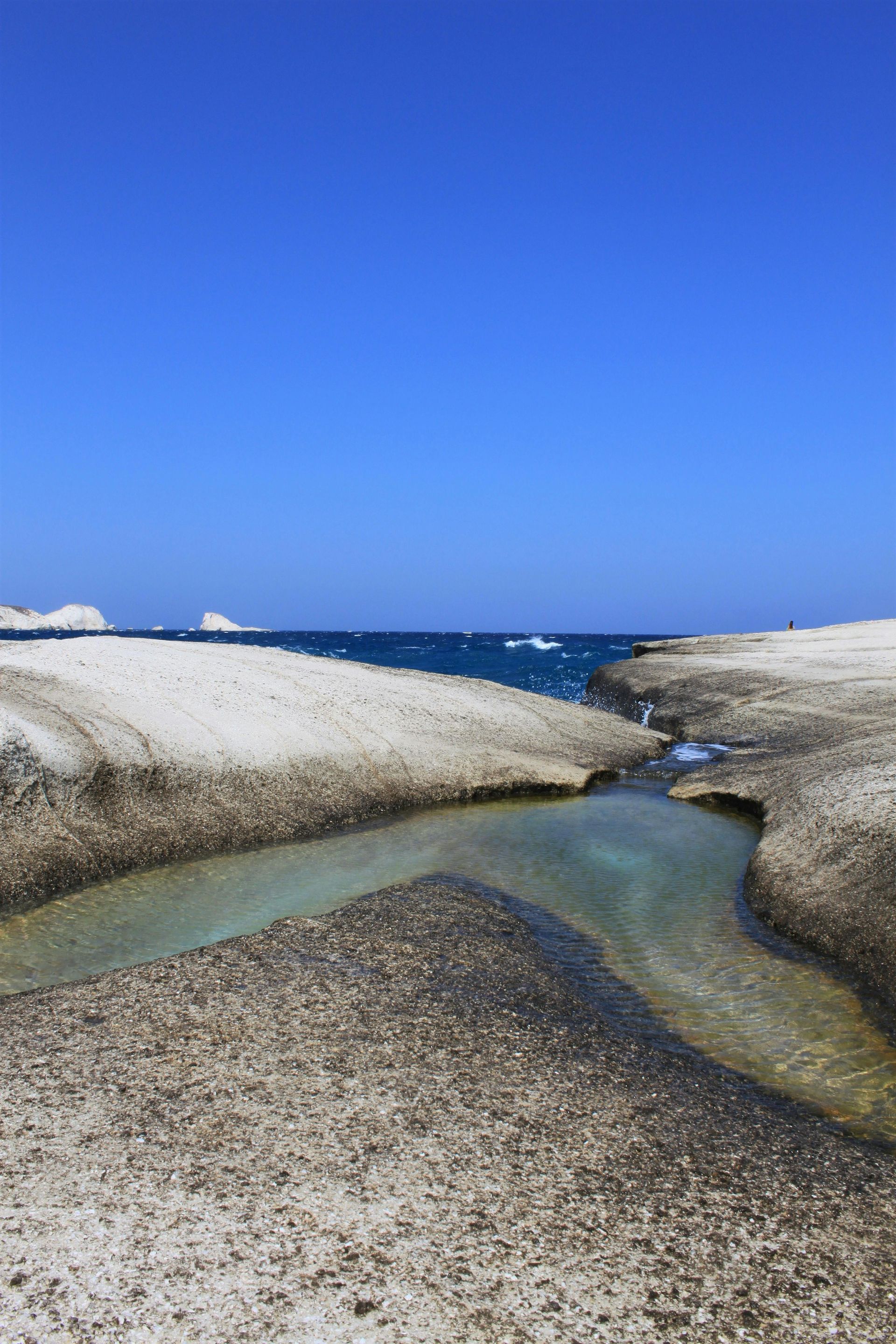 A small stream runs through a rocky area on Sarakiniko Beach in Milos, Greece.